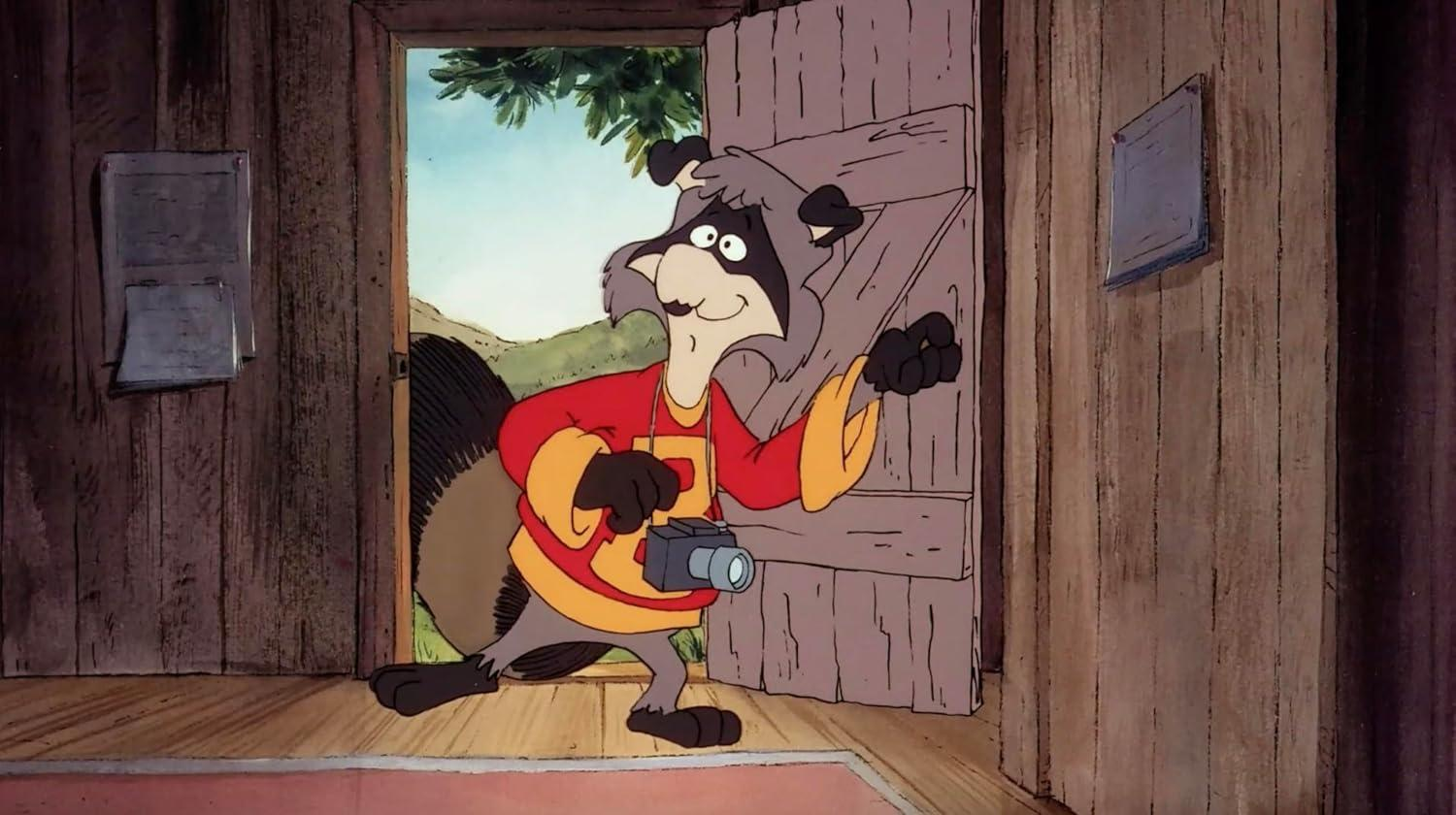 Ein Cartoon-Waschbär mit Kamera steht in einer Tür. Er trägt ein rotes Hemd und einen grauen Kopf. Holztür und Wand im Hintergrund.