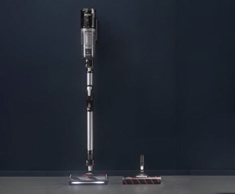 Bezprzewodowy odkurzacz stoi obok odłączanej głowicy, na tle ciemnoniebieskiej ściany i szarej podłogi.