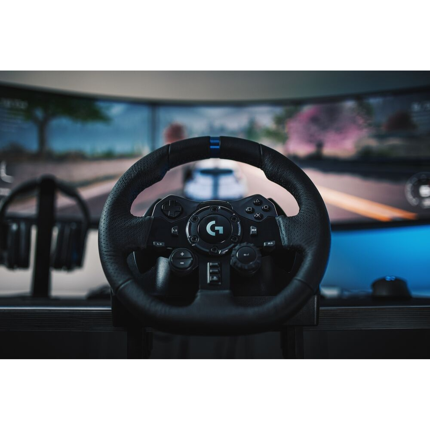 Un volante da corsa Logitech nero è a fuoco. Sullo sfondo c'è uno schermo che mostra un gioco di corse. Sono visibili altri accessori di gioco.