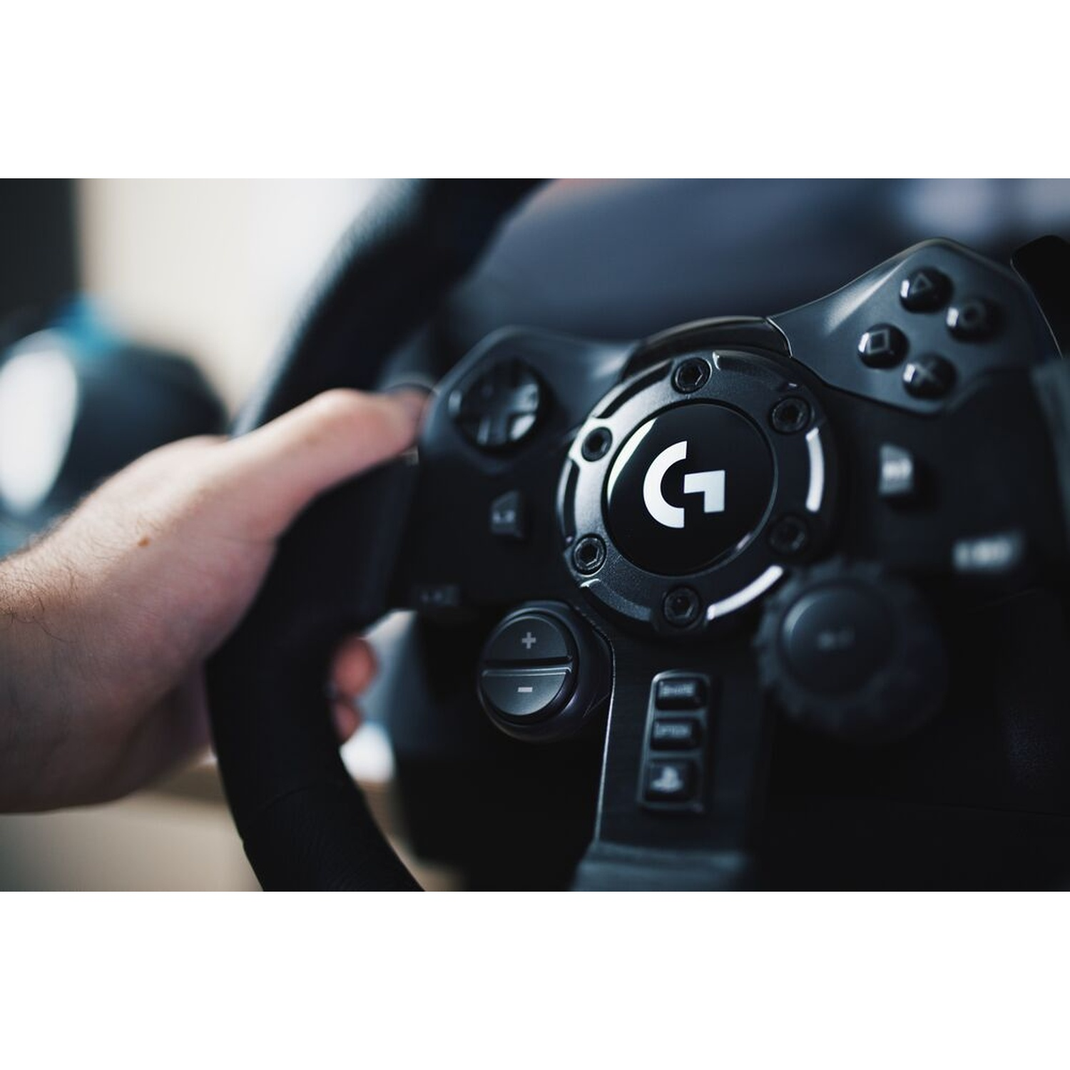 Una mano afferra un volante nero con il logo Logitech. Pulsanti e comandi sono visibili sul volante. Lo sfondo è sfocato.
