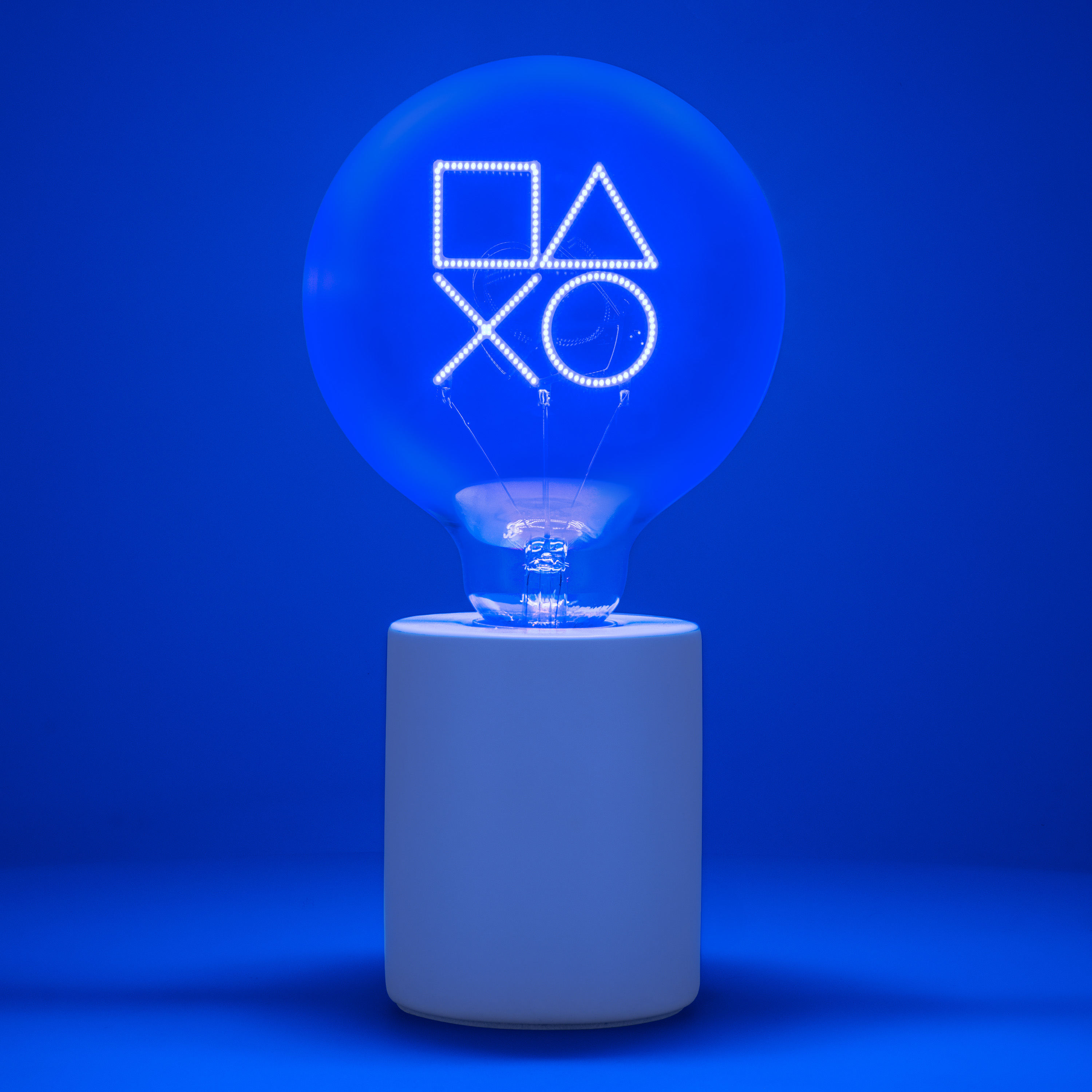 Eine Glühbirne mit PlayStation-Symbolen leuchtet auf weißem Sockel vor blauem Hintergrund.