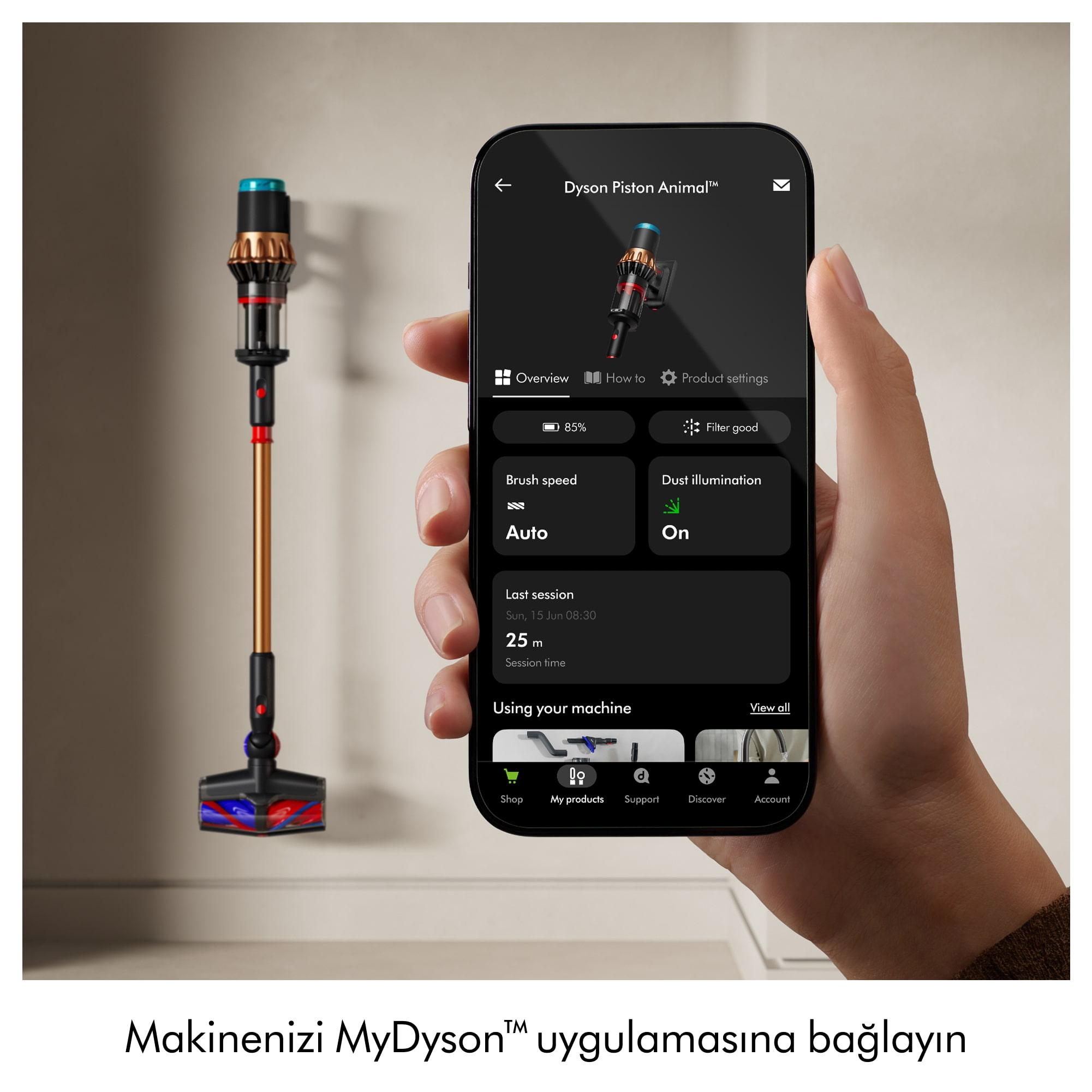 Dyson Piston Animal elektrikli süpürgesini gösteren bir telefon tutan el. Telefonun yanında başka bir elektrikli süpürge duruyor.