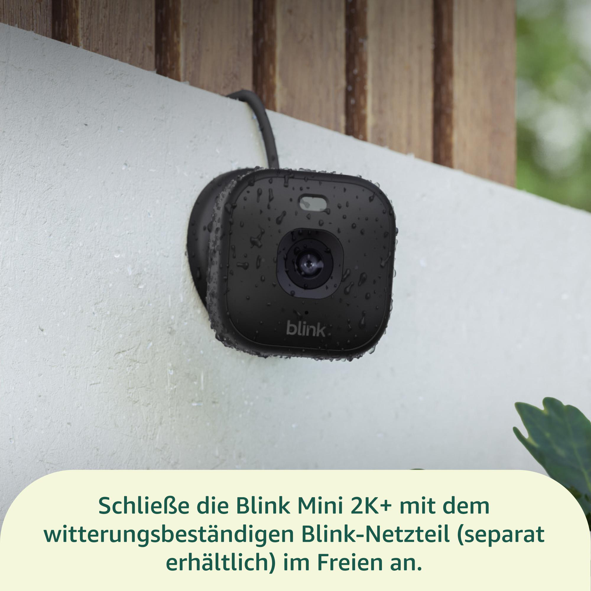 Schwarze Blink Mini 2K+ Überwachungskamera an einer weißen Wand mit Tropfen. Holzbretter im Hintergrund.