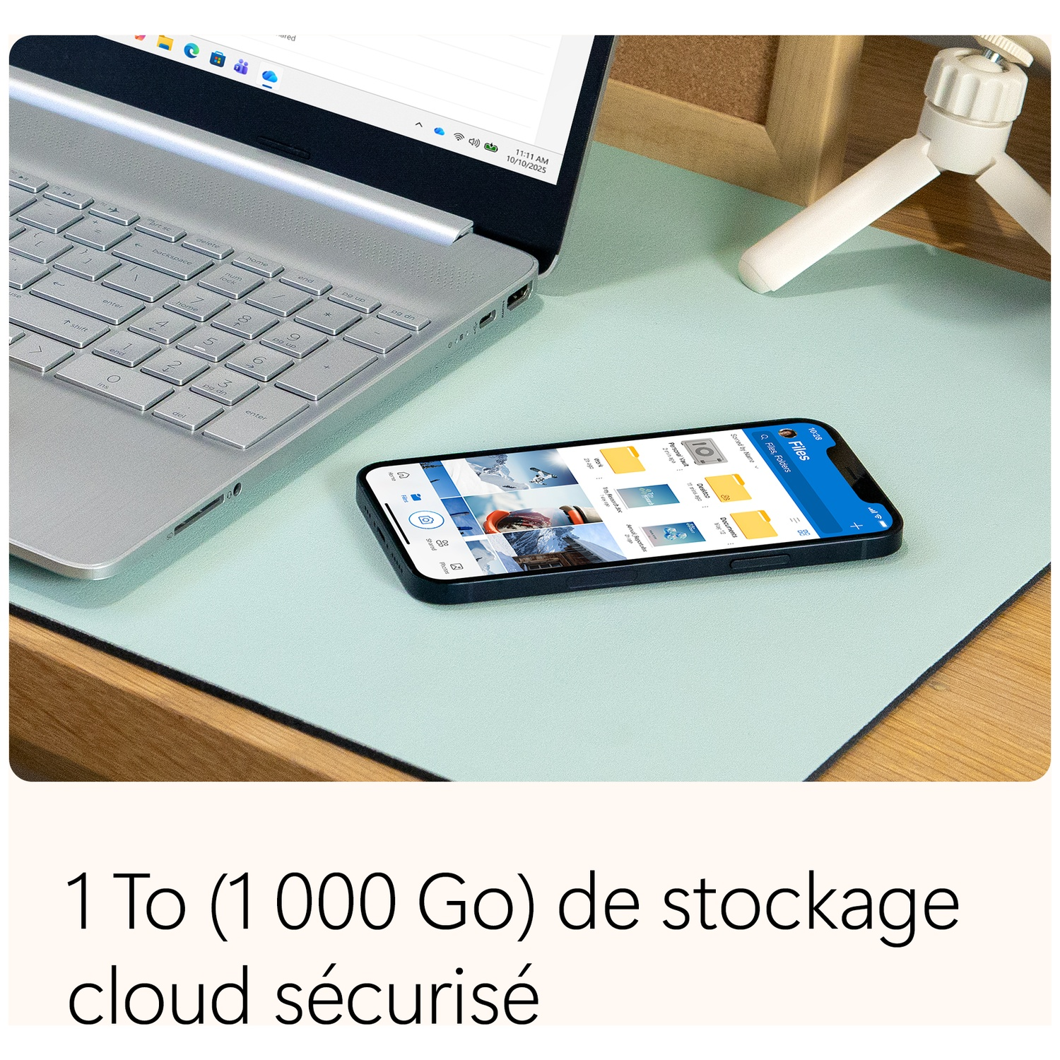 Ordinateur portable, téléphone avec application de fichiers et petit trépied sur un bureau. Le texte en dessous est '1 To (1 000 Go) de stockage cloud sécurisé'.