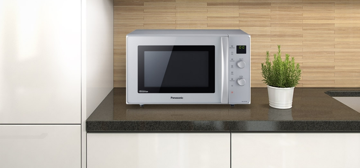 Srebrna kuchenka mikrofalowa Panasonic na blacie, z małą rośliną w białej doniczce.