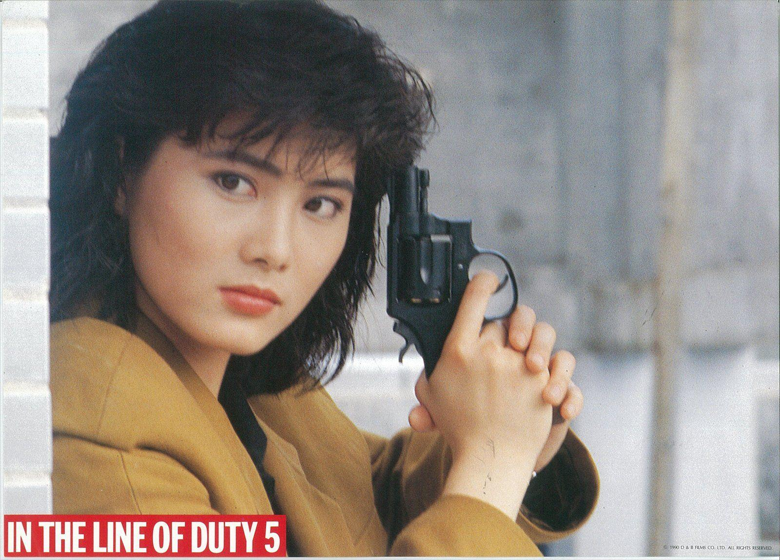 Eine Frau hält eine Waffe und blickt in die Kamera. Sie trägt eine gelbe Jacke. Unten steht "IN THE LINE OF DUTY 5".