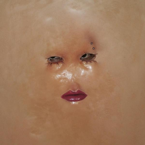 Nahaufnahme eines Gesichts mit braunen Augen, langen Wimpern und roten Lippen. Ein Piercing über dem linken Auge. Die Haut ist hell und glatt.