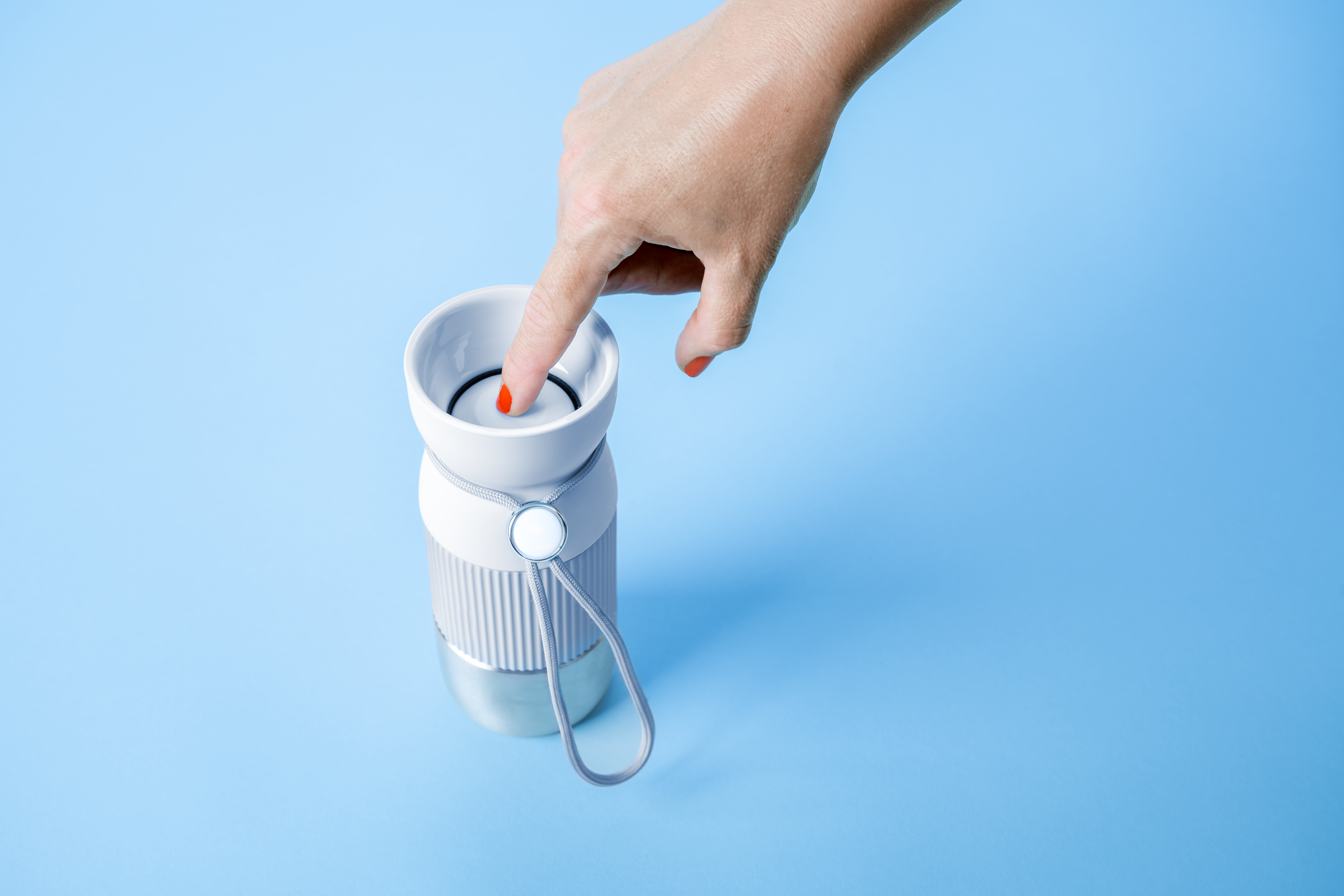 Eine Hand drückt einen roten Knopf auf einer weiß-grauen Wasserflasche. Der Hintergrund ist hellblau.