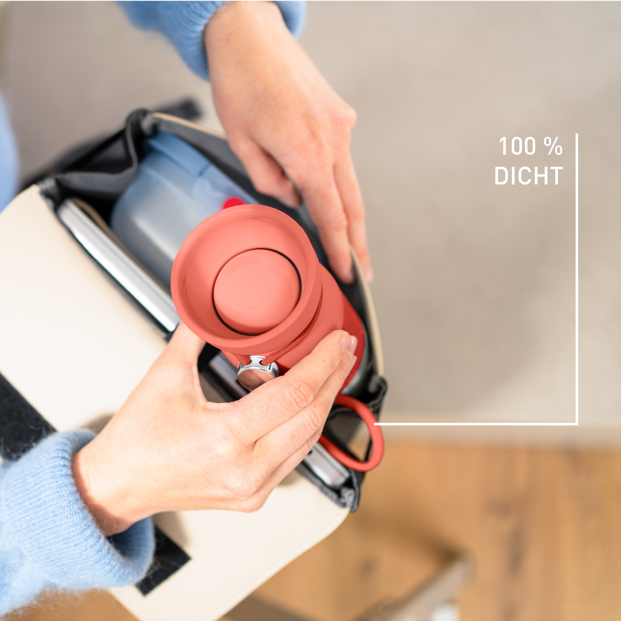 Hände halten einen lachsfarbenen Lautsprecher in einer Tasche. Der Text '100% dicht' ist sichtbar.