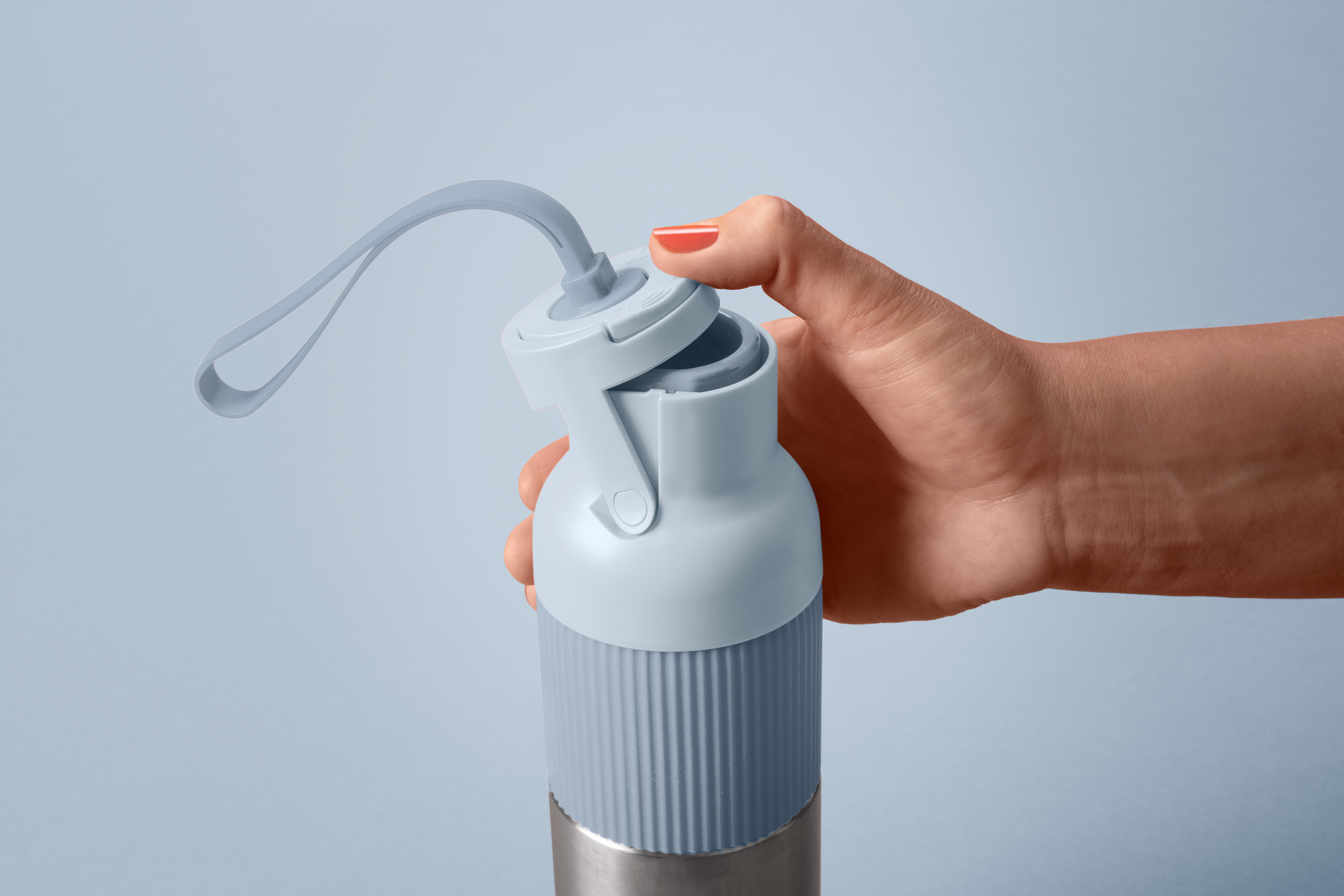 Eine Hand hält eine hellblaue Wasserflasche mit einem grauen Riemen. Die Hand hat roten Nagellack. Der Hintergrund ist einfarbig hellblau.