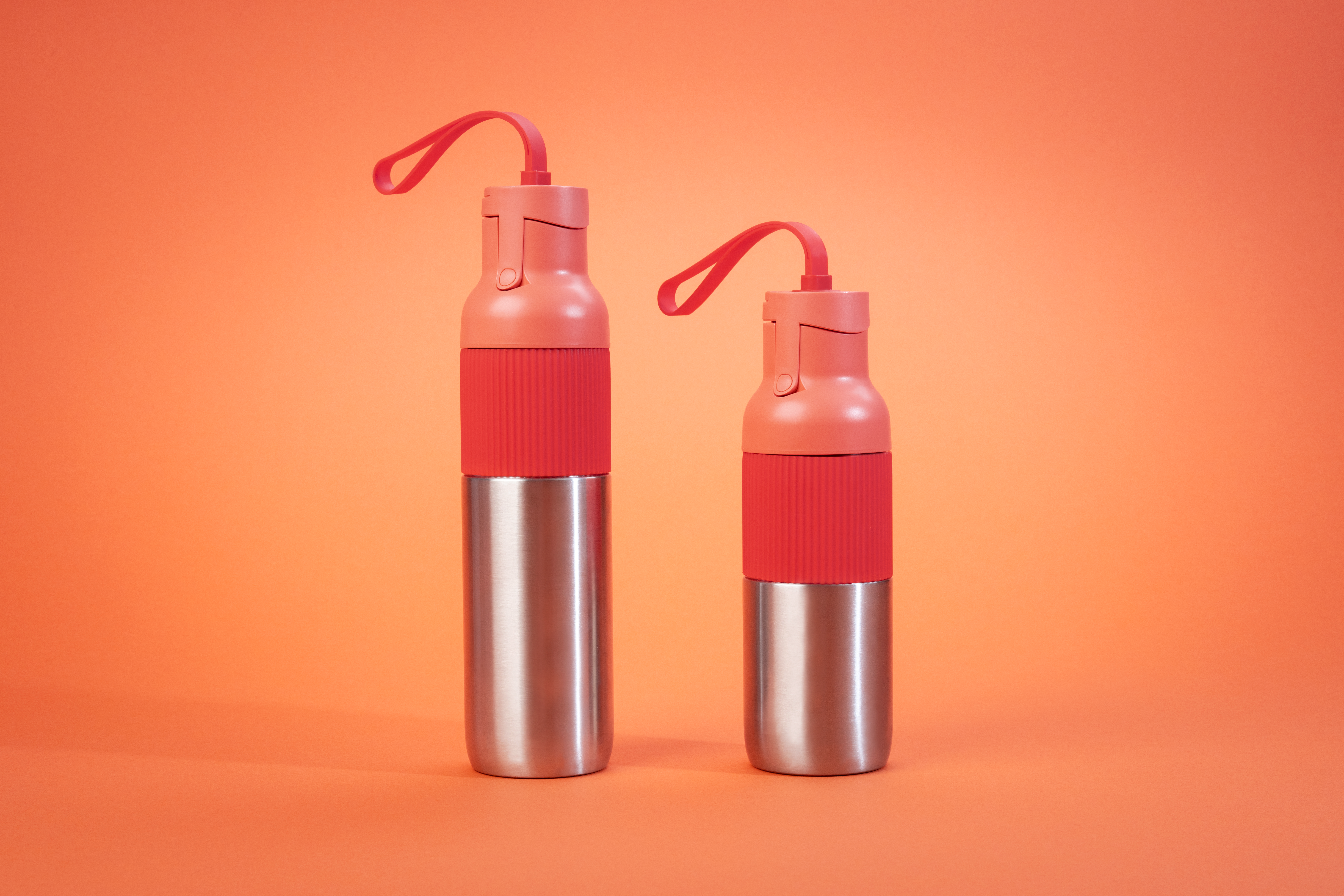 Zwei Wasserflaschen mit roten, rosa und silbernen Teilen. Sie stehen auf einem orangen Hintergrund mit Schlaufengriffen.