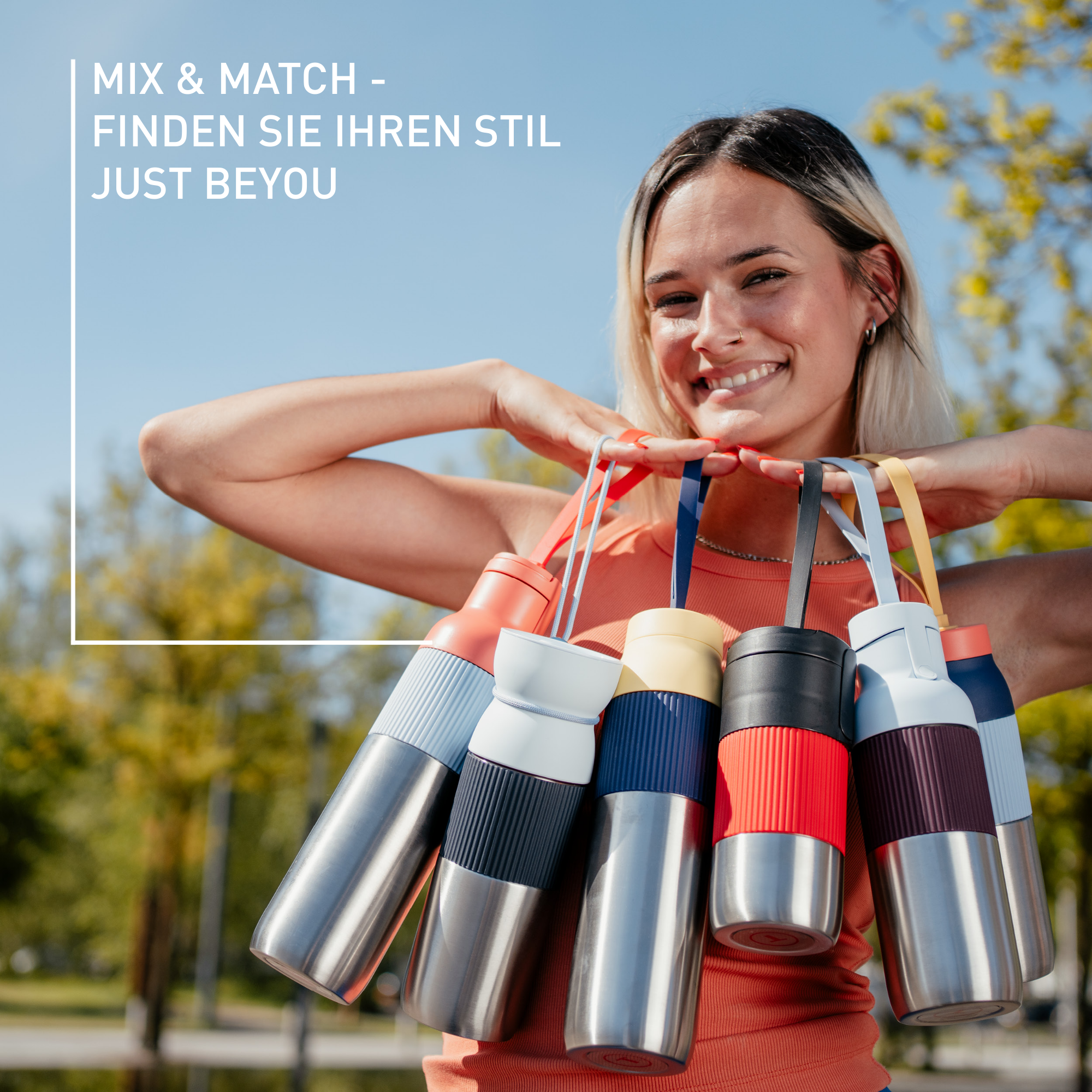 Lächelnde Frau, die verschiedene bunte Wasserflaschen hält. Blauer Himmel und Bäume im Hintergrund. Text: 'Mix & Match'.