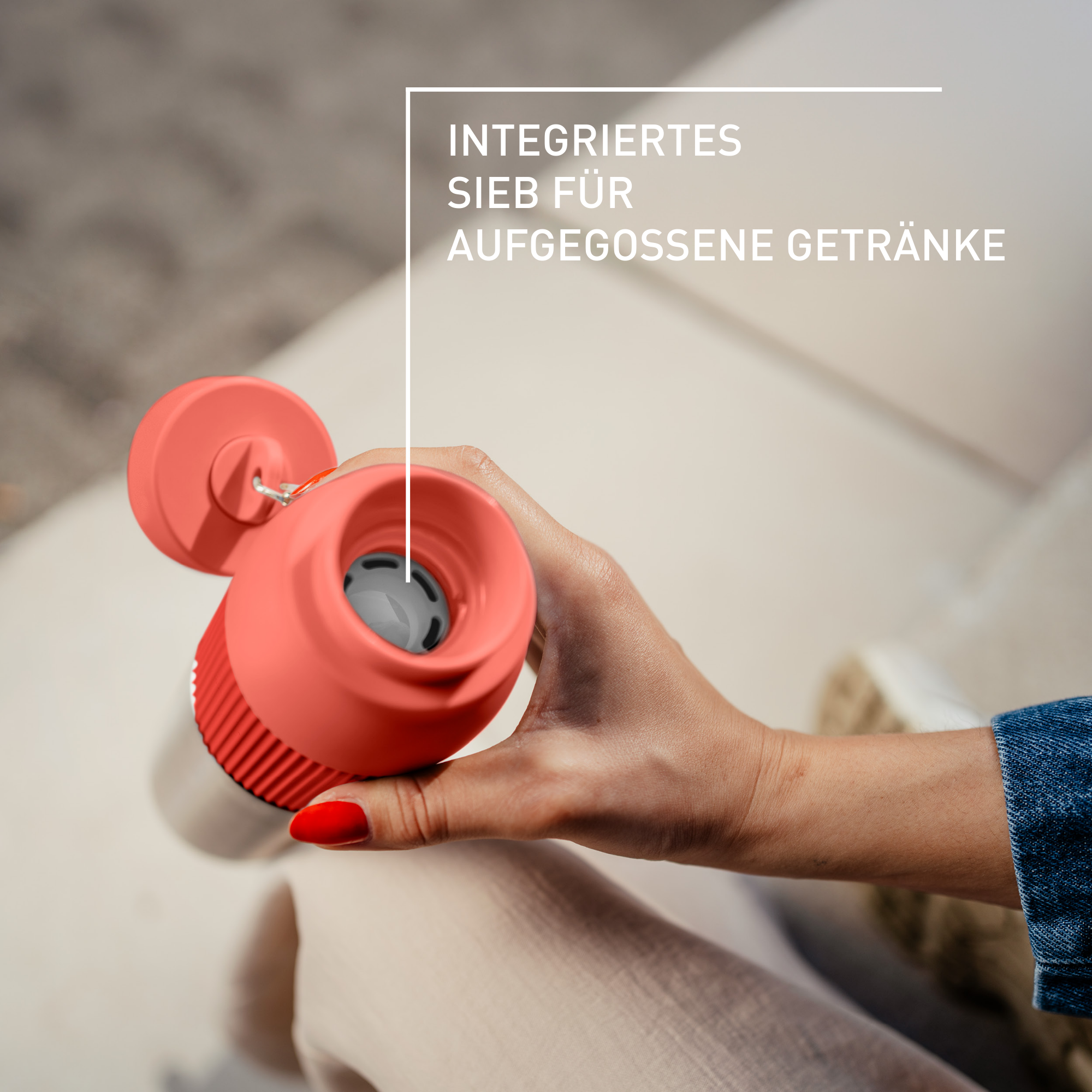 Eine Person hält eine rote Wasserflasche. Die Flasche hat einen roten Deckel und einen grauen Filter. Roter Nagellack.