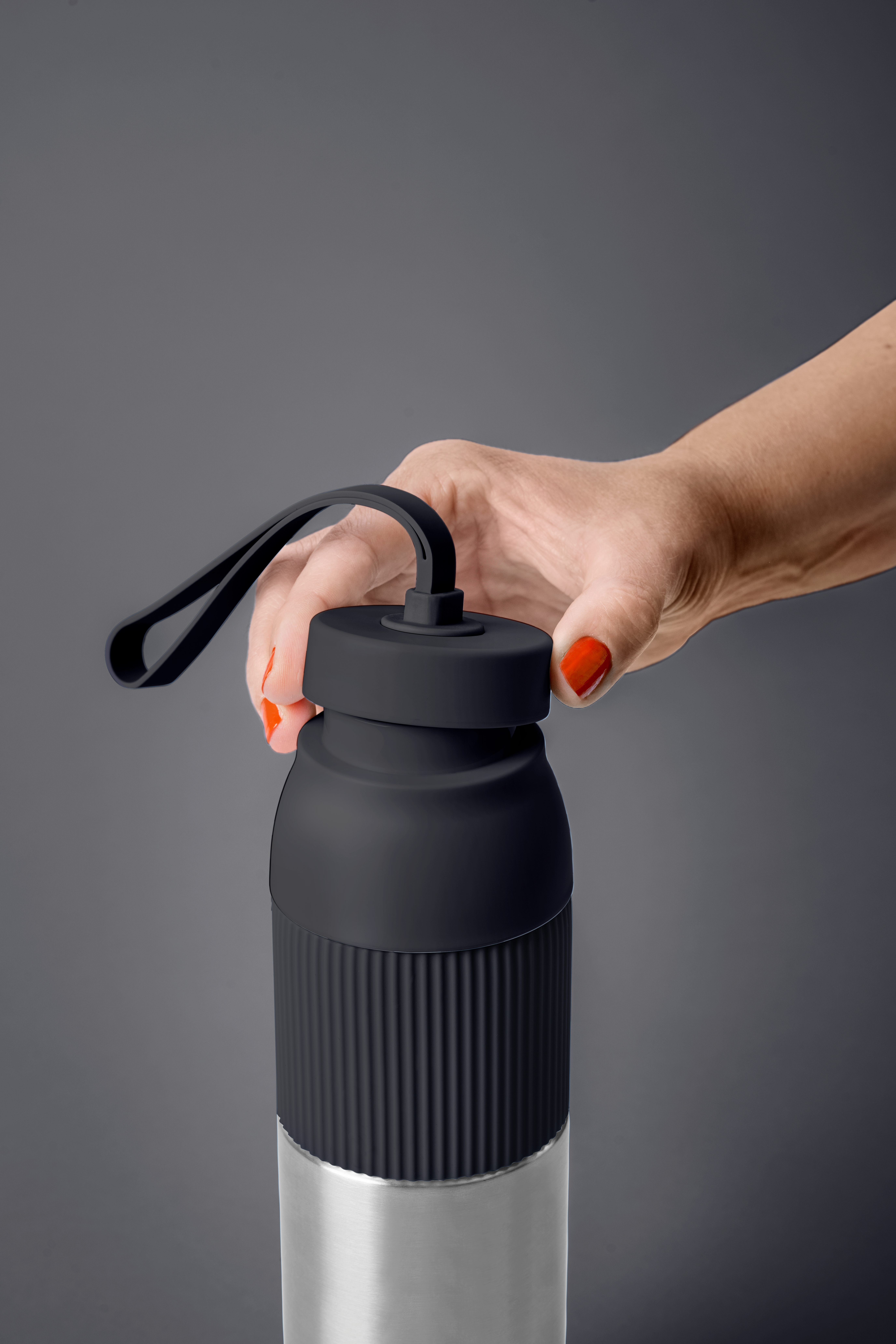 Eine Hand mit roten Nägeln hält eine schwarze Wasserflasche. Die Flasche ist unten silberfarben und hat einen schwarzen Deckel.