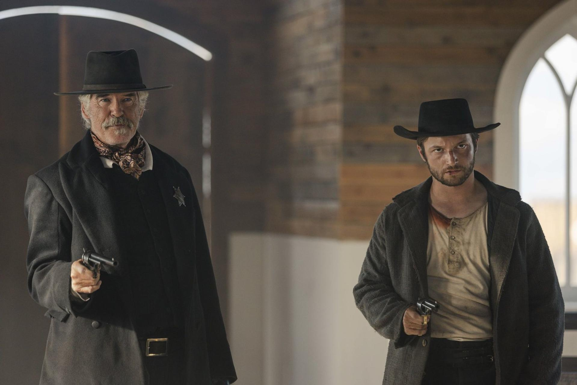 Zwei Männer mit Cowboyhüten halten Waffen. Einer trägt einen Mantel, der andere ein blutbeflecktes Hemd. Hintergrund zeigt ein Gebäudeinneres.