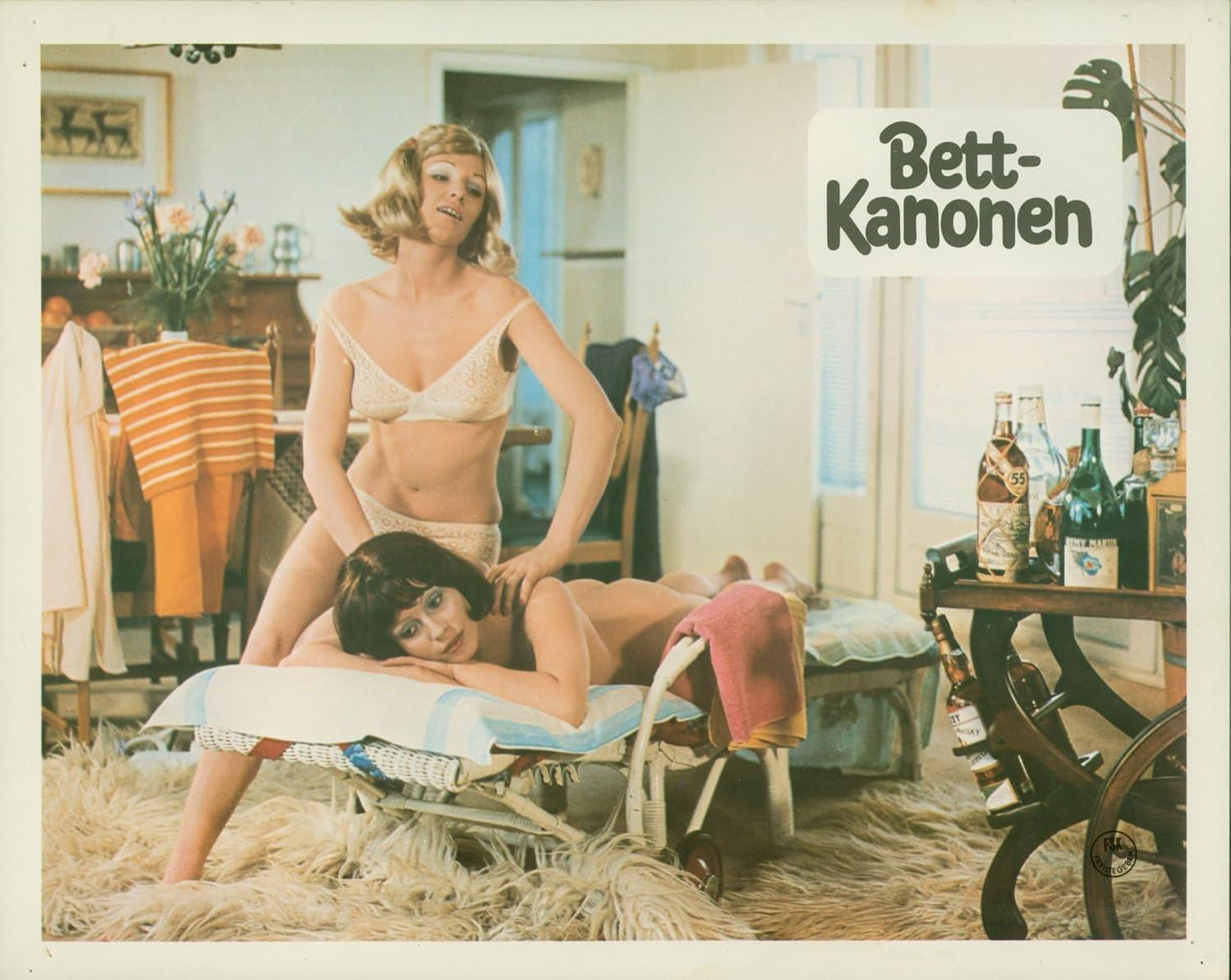 Zwei Frauen, eine massiert den Rücken der anderen. Flaschen und ein Schild mit der Aufschrift "Bett-Kanone" sind im Hintergrund. Ein flauschiger Teppich.