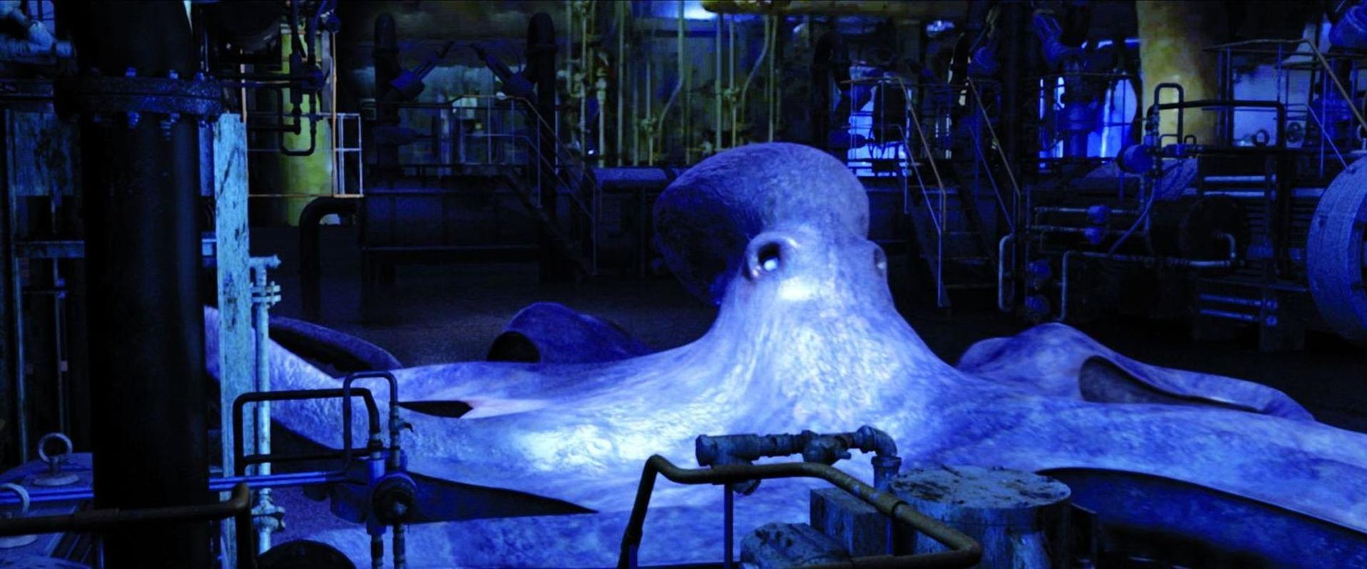 Ein großer blauer Oktopus in einer Industrieumgebung. Rohre und Maschinen umgeben das Tier. Die Szene ist schwach beleuchtet.