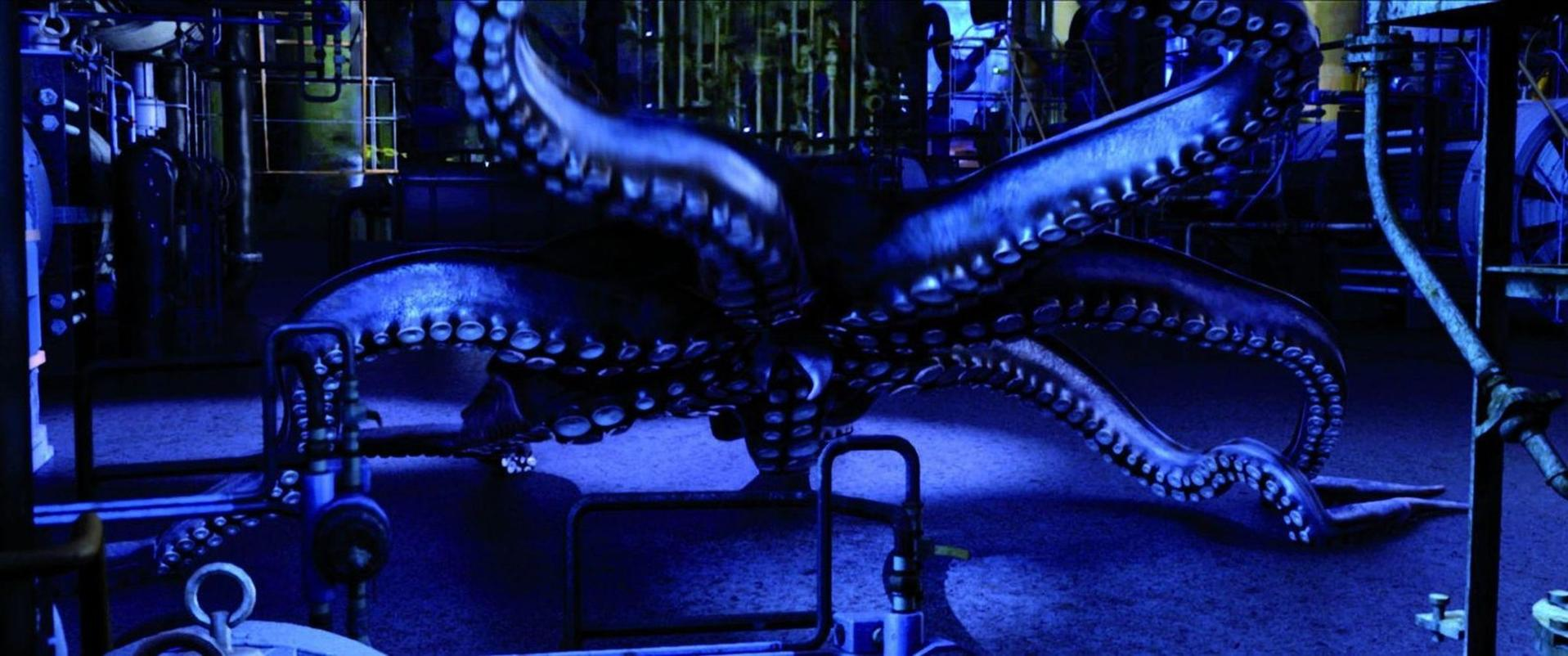 Ein großer Oktopus mit blauer Haut befindet sich in einer dunklen Industrieumgebung. Seine Tentakel verteilen sich auf Rohre und Geräte.