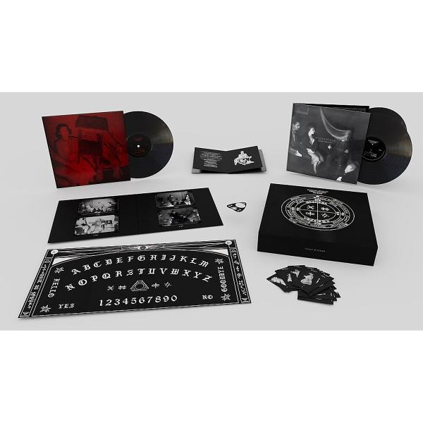 Eine Sammlung von Schallplatten, ein Ouija-Brett, eine Box und Karten werden auf einer weißen Oberfläche präsentiert. Die Artikel sind schwarz und rot.