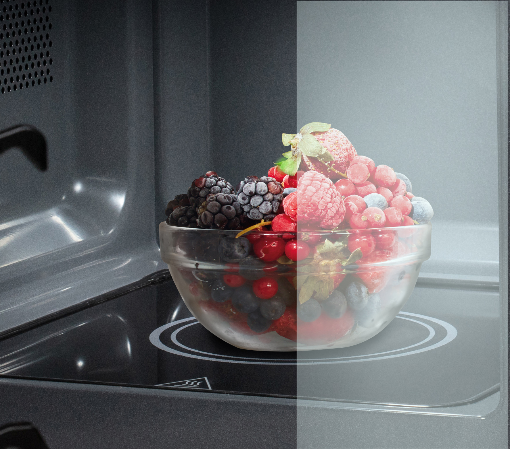 Eine Glasschüssel mit gefrorenen Beeren steht in einer Mikrowelle. Zu den Beeren gehören Blaubeeren, Himbeeren, Erdbeeren und Johannisbeeren.