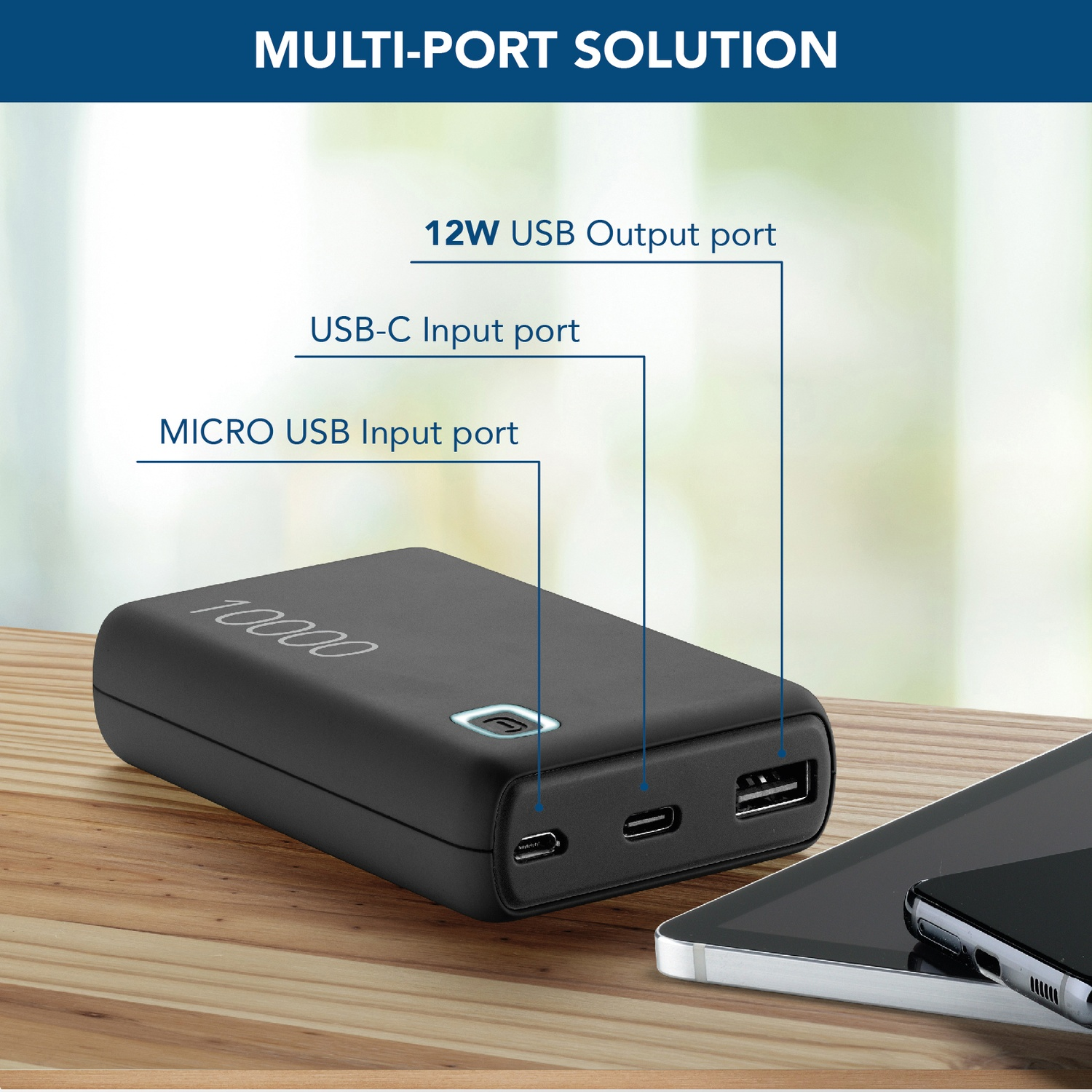 Power bank nera con porte USB, un tablet e un telefono su una superficie di legno. Il testo etichetta le porte.