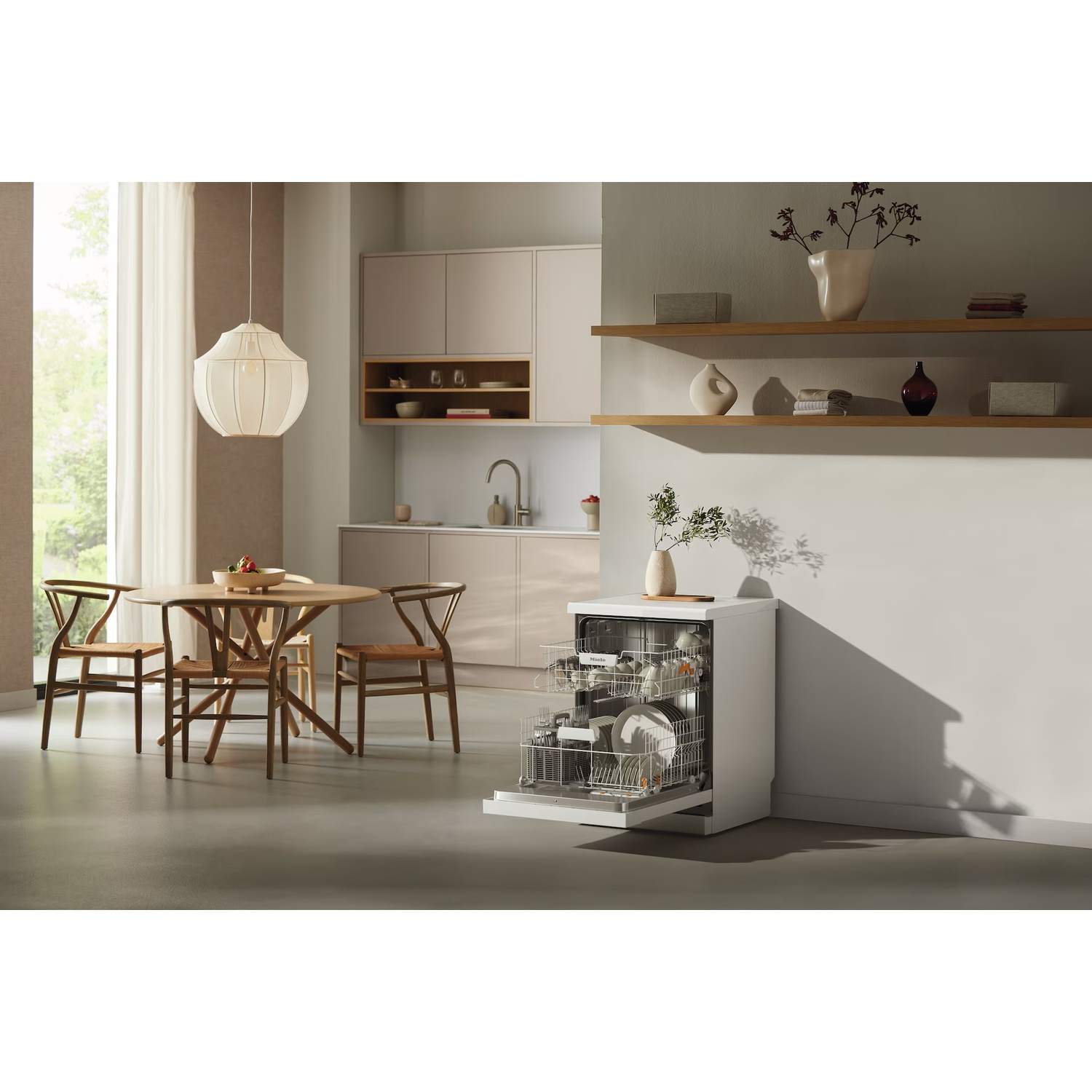 A kitchen scene with a white dishwasher open, wooden table and chairs, and decorative items on shelves. A window is in the background.