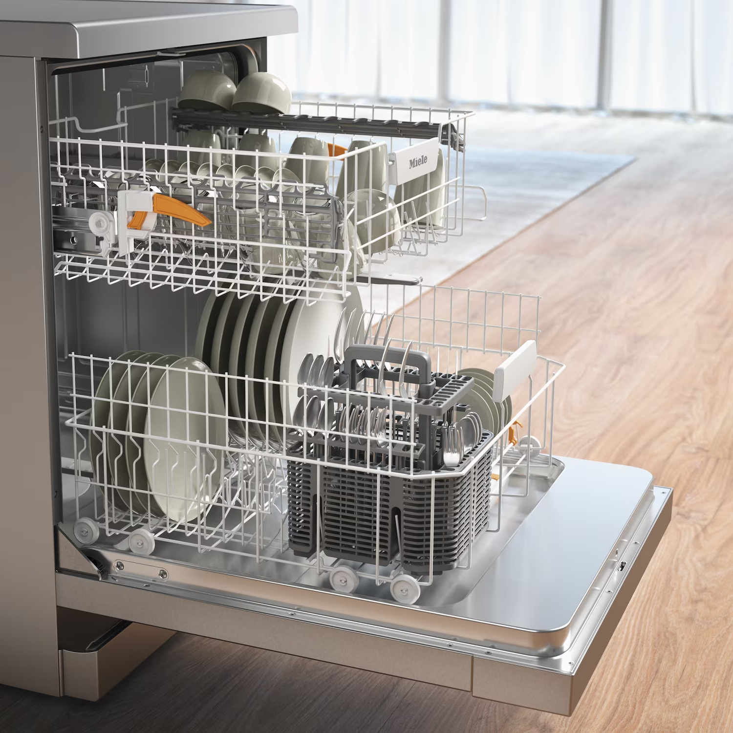 Open dishwasher with dishes inside. Plates, cups, cutlery in racks. Wooden floor and window in the background.