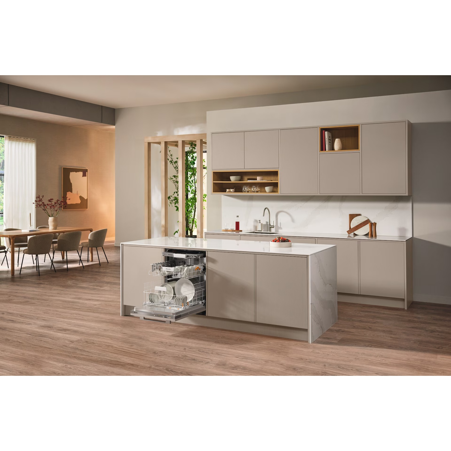Cuisine moderne avec lave-vaisselle ouvert, rempli de vaisselle. Îlot, armoires, table à manger visible. Plancher en bois.