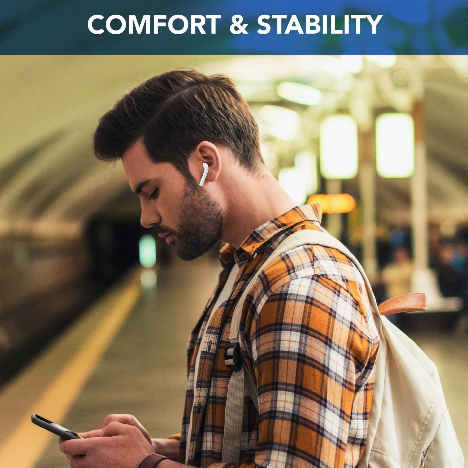 Un uomo con camicia a quadri, auricolari, zaino e telefono in una stazione della metropolitana. Il testo Comfort & Stability è in alto.