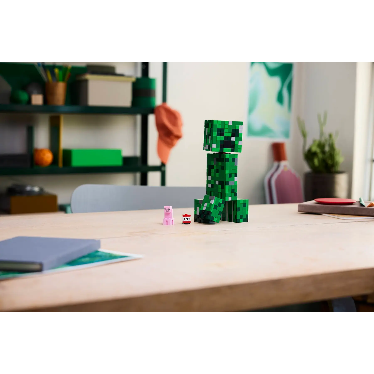 Een Minecraft-scène met een groene Creeper, een roze varken en TNT op een houten tafel. Een plank met objecten op de achtergrond.