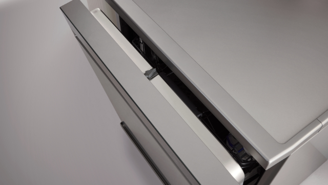 Zbliżenie srebrnych drzwi zmywarki lekko uchylonych, ukazujących elementy wewnętrzne i jasnoszare tło.