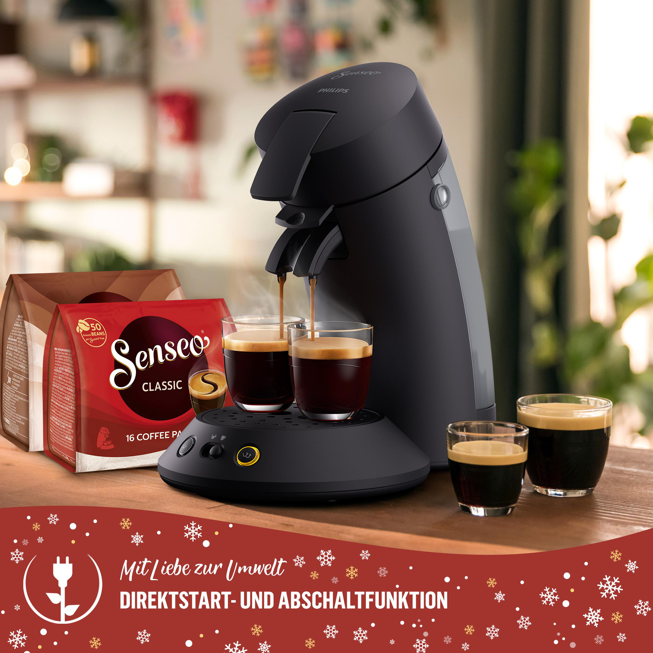 Eine schwarze Kaffeemaschine mit zwei Kaffeetassen, Kaffeepäckchen und Text auf rotem Hintergrund mit Schneeflocken.