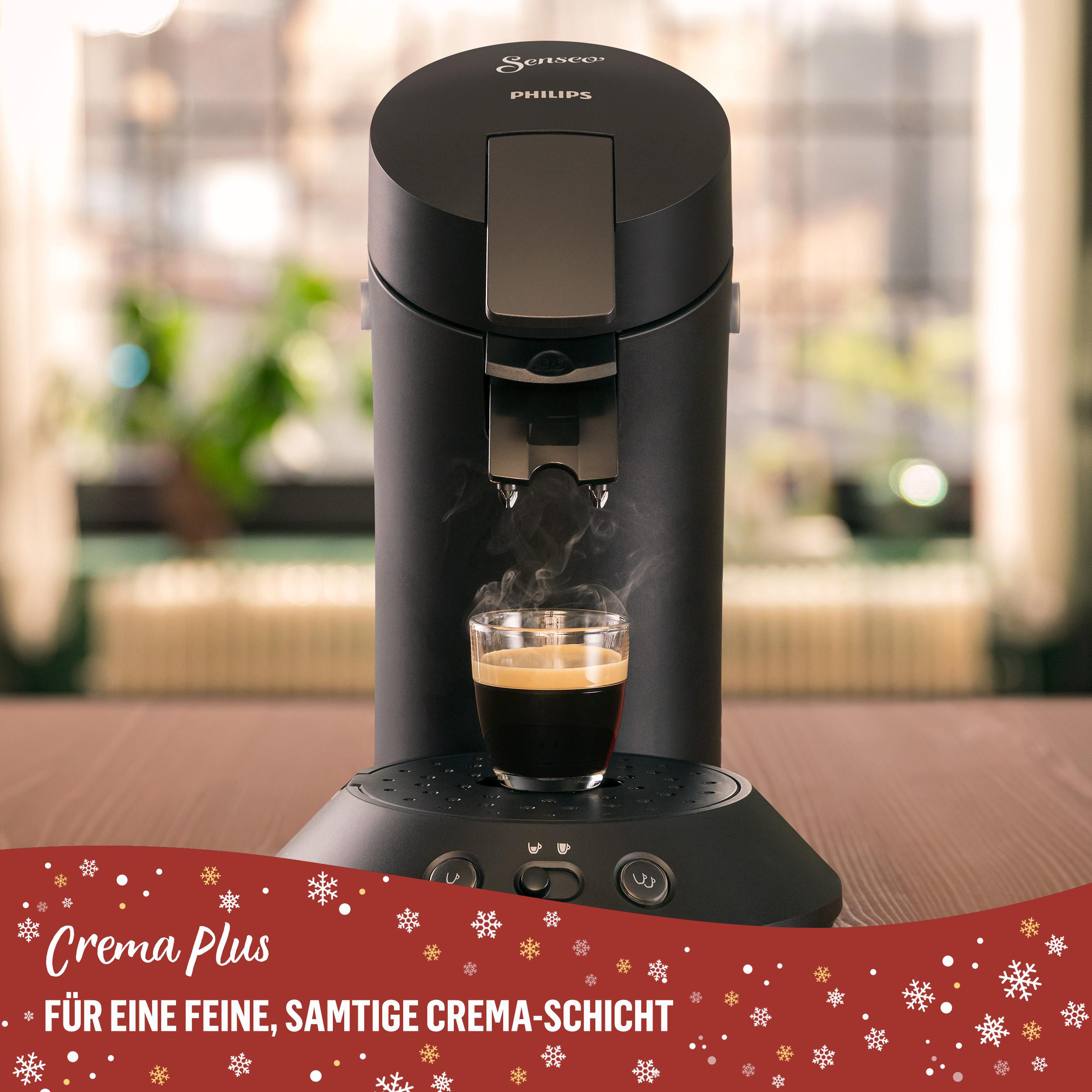 Eine schwarze Philips Senseo Kaffeemaschine mit einem Glas Kaffee. Dampf steigt auf. Roter Feiertagshintergrund.