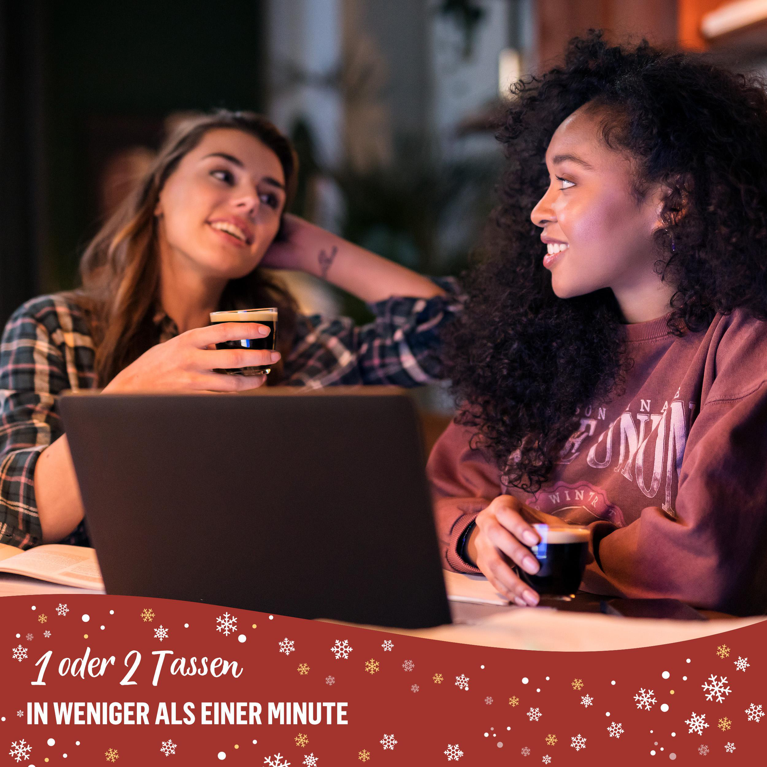 Zwei Frauen sitzen mit Kaffee an einem Tisch. Eine schaut die andere an. Ein Laptop liegt ebenfalls auf dem Tisch.