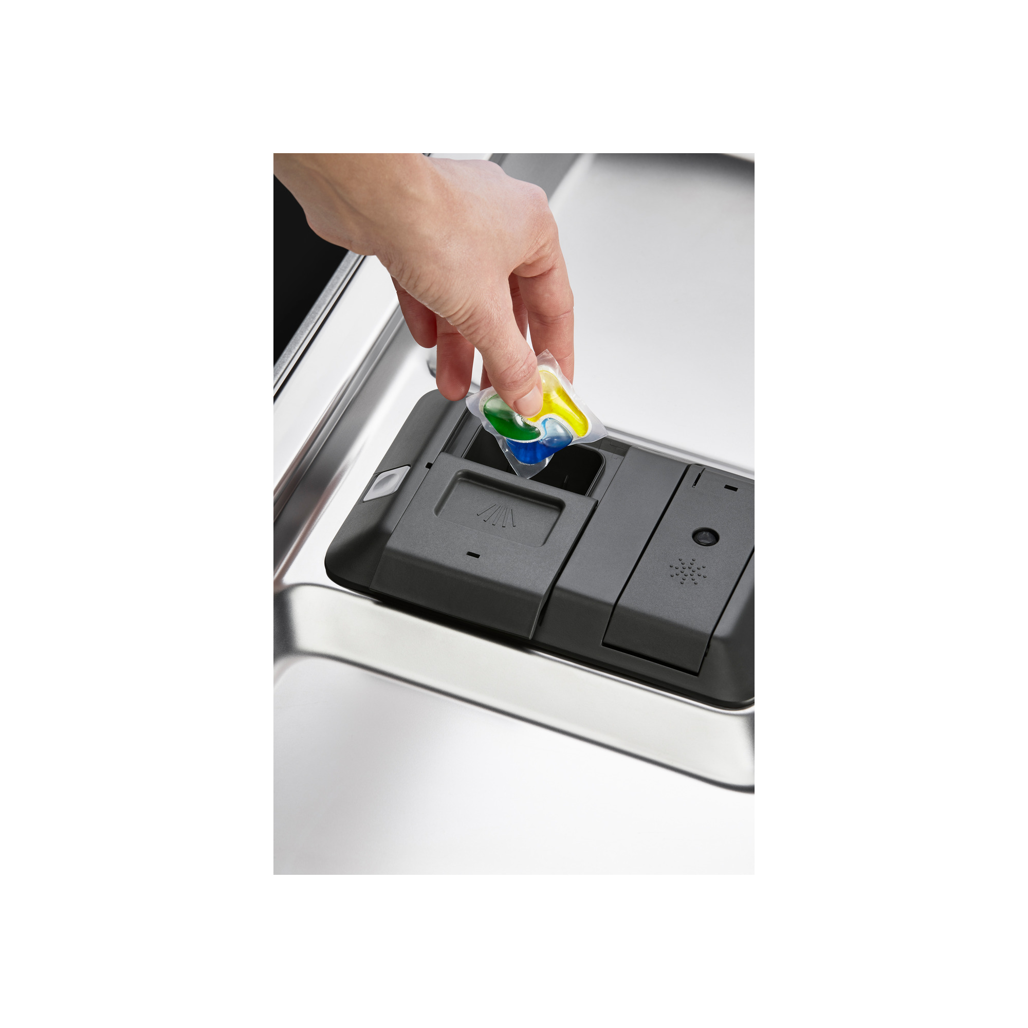 Ręka umieszcza kapsułkę z detergentem do zmywarki w dozowniku. Dozownik jest czarny, a zmywarka ze stali nierdzewnej.