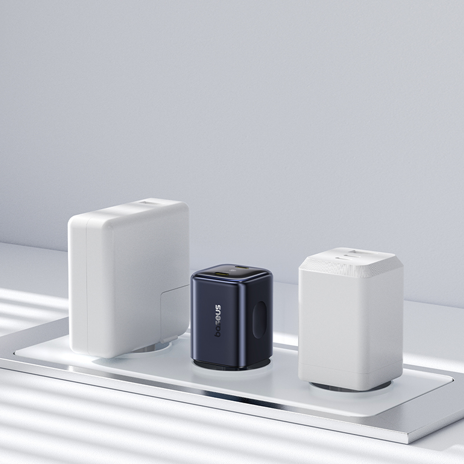 Tres adaptadores de corriente en una superficie blanca. Uno es blanco, otro negro con "baseus" y el último es blanco.