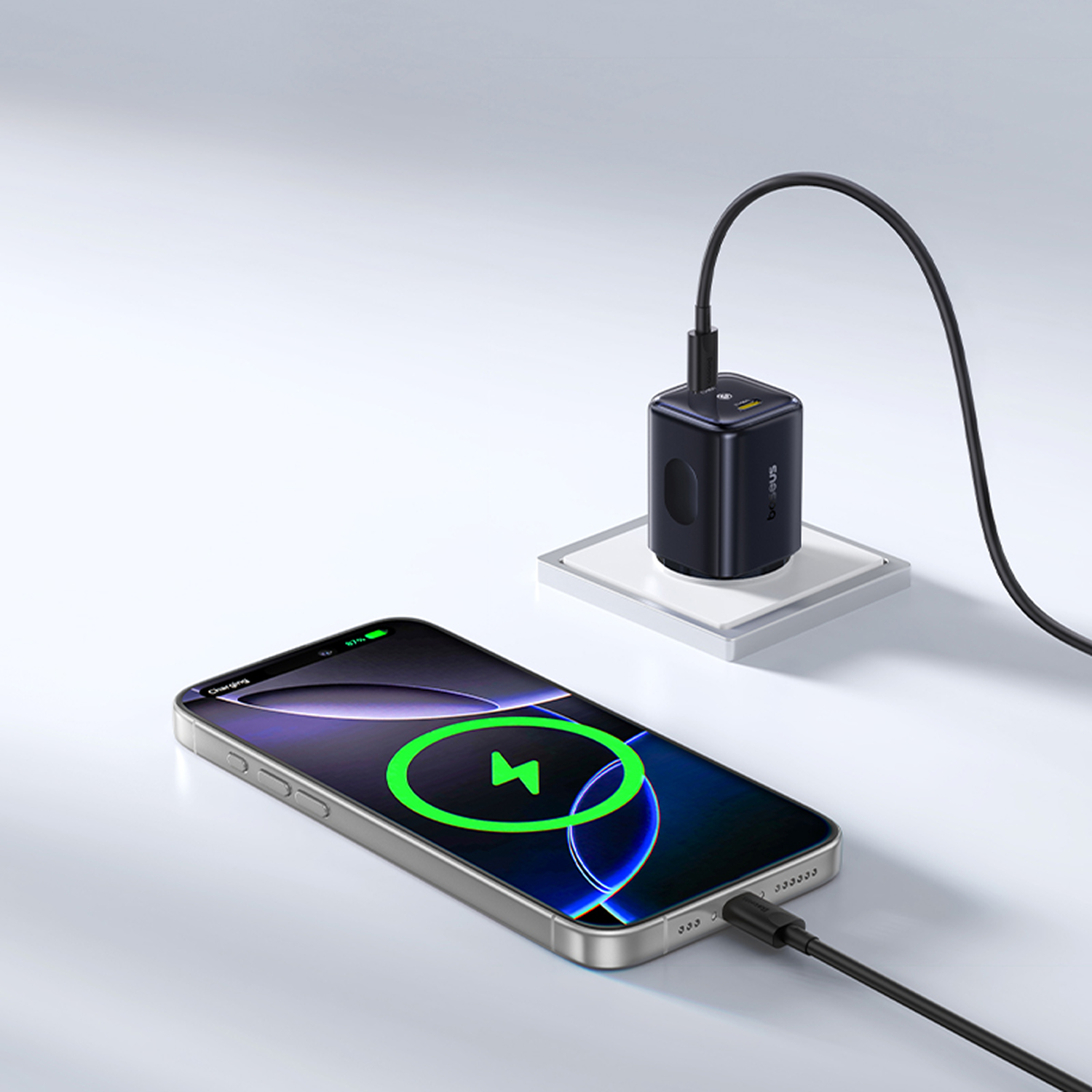 Un teléfono se está cargando con un cargador negro. El teléfono es plateado con un símbolo de carga. El cargador está en una base blanca.