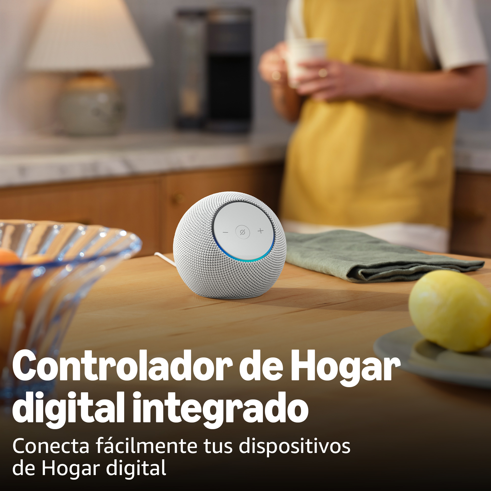 Un altavoz inteligente sobre una mesa de madera. Una persona de amarillo sostiene una taza. Un limón y un plato están en la mesa.