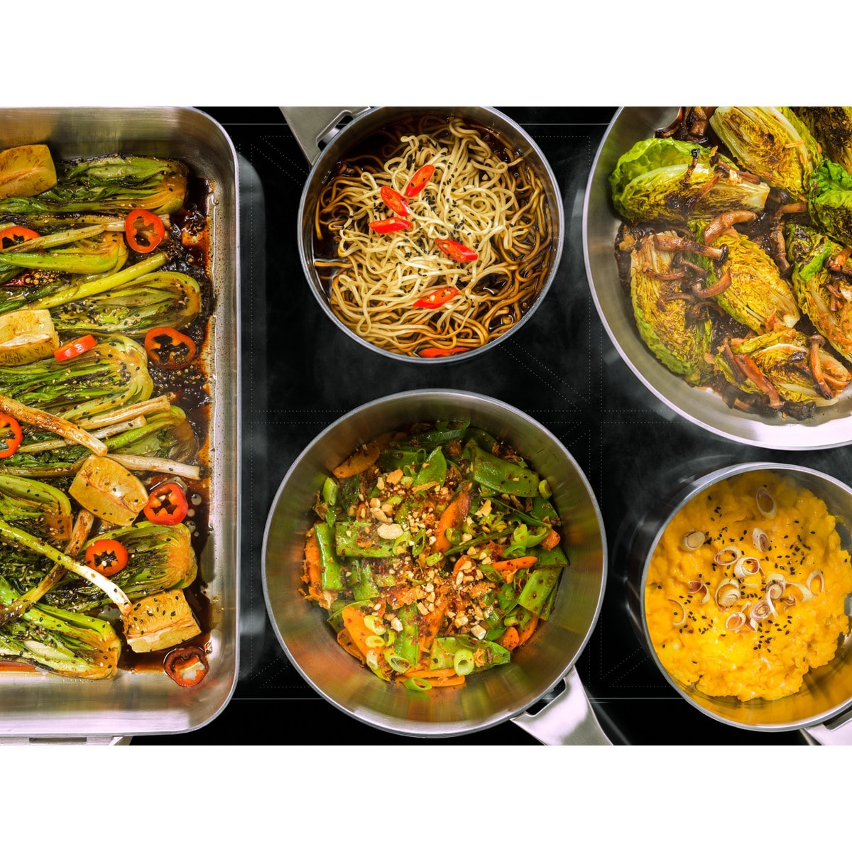 Vista cenital de varios platos: bok choy, fideos, coles de Bruselas y otras verduras en ollas sobre una estufa negra.