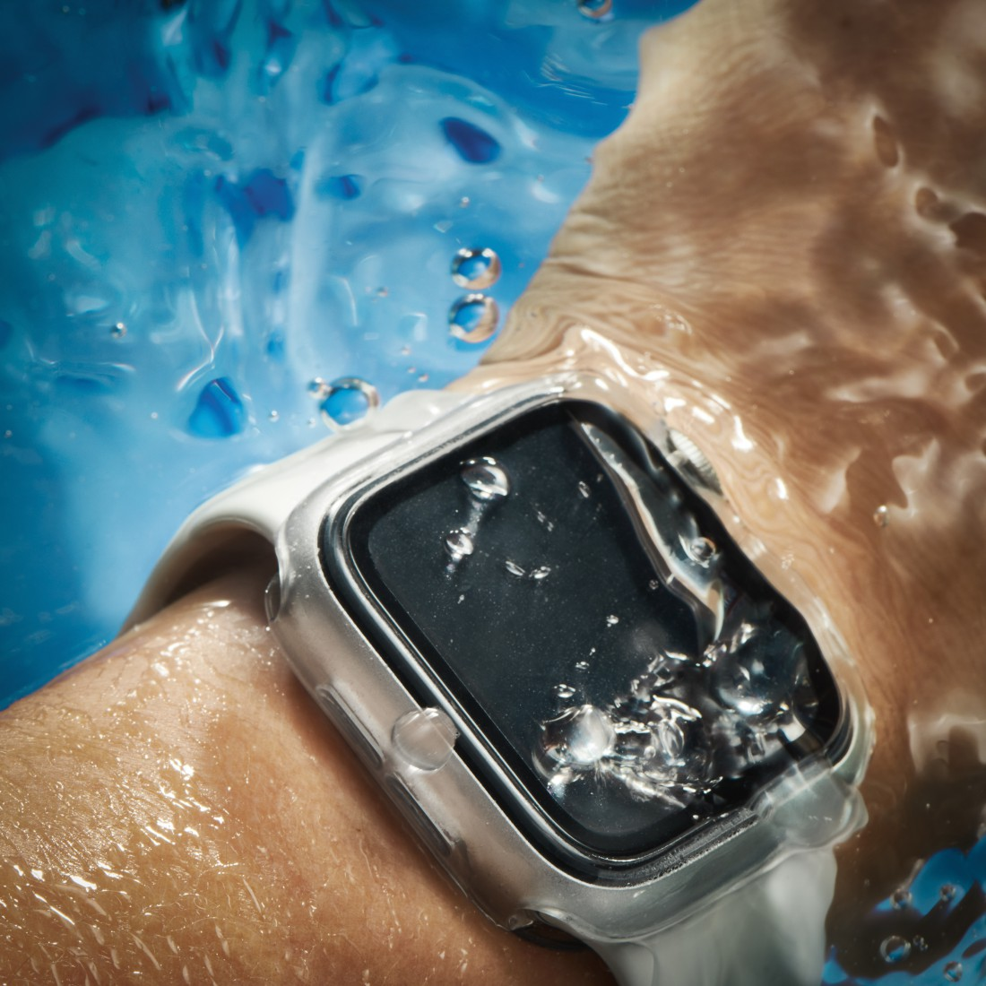 Ein Handgelenk mit einer weißen Smartwatch, die in blaues Wasser getaucht ist. Wassertropfen auf dem Ziffernblatt und dem Handgelenk.