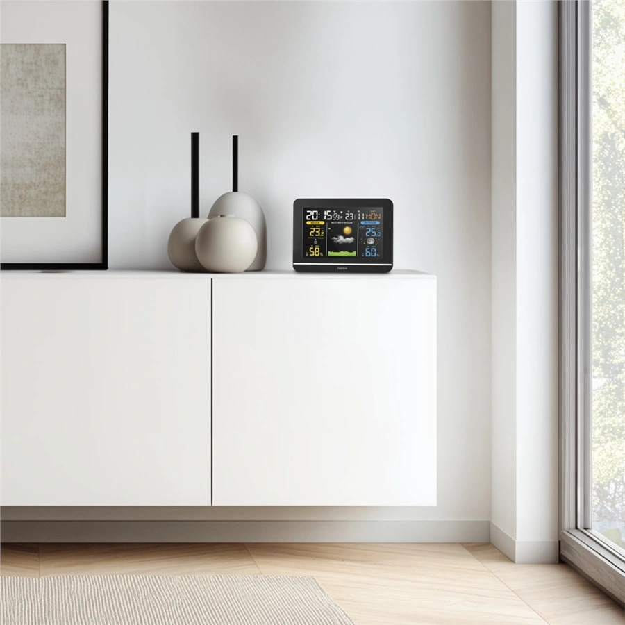 Stacja pogodowa stoi na białej szafce. Ozdobne wazony są po lewej stronie. Po prawej stronie znajduje się okno. Na podłodze leży dywan.