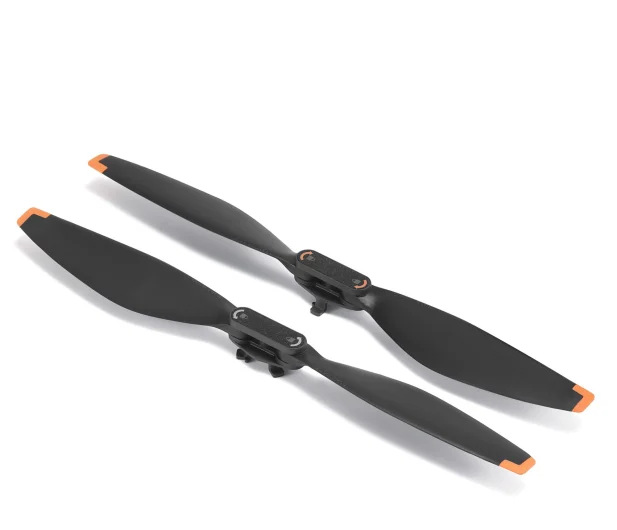 Dwie czarne śmigła drona z pomarańczowymi końcówkami leżą na białej powierzchni. Są ustawione pod kątem, ukazując kształt i detale.