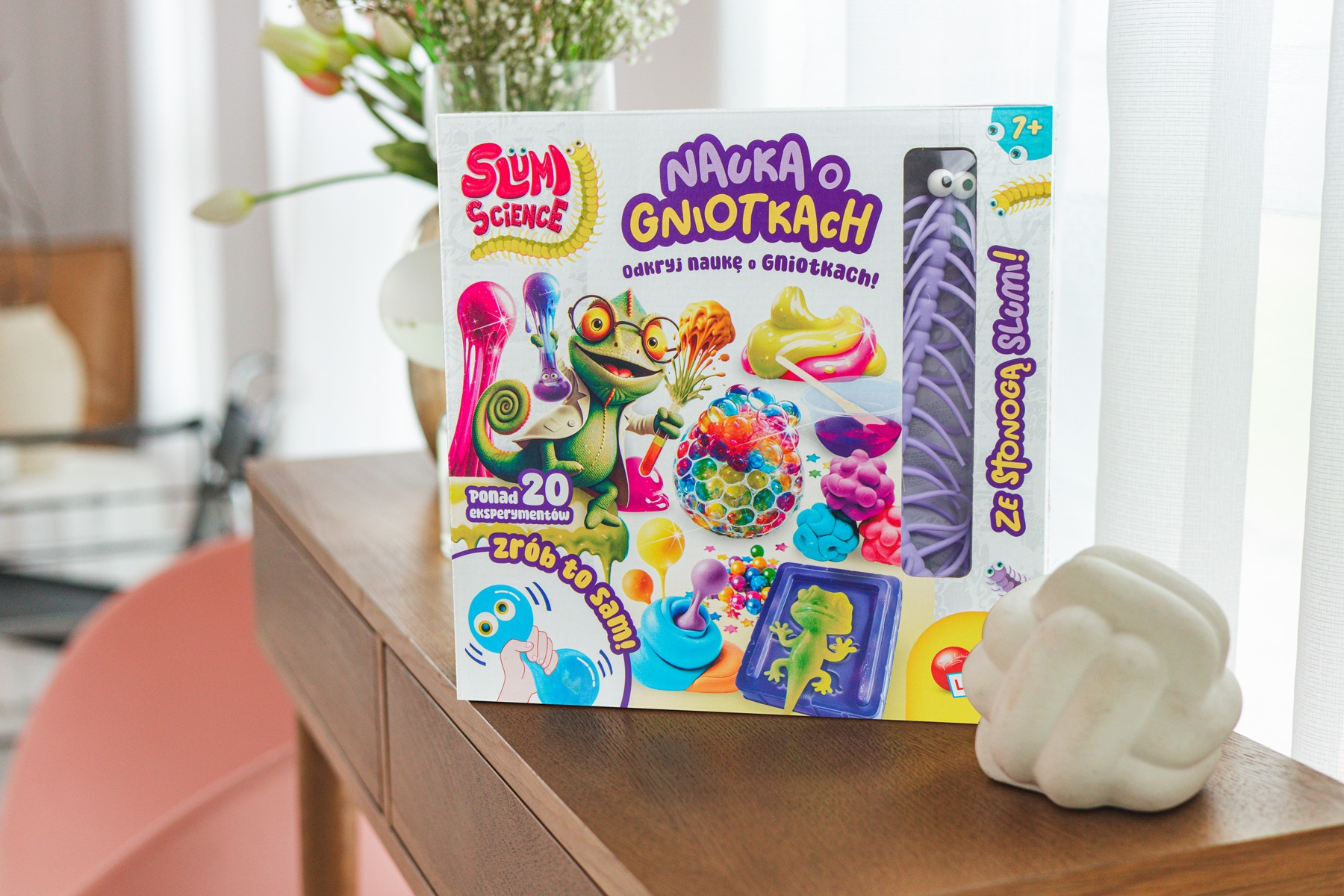 Zestaw pudełek na drewnianym stole. Pudełko przedstawia postacie z kreskówek i tekst w języku polskim. Biała rzeźba na pierwszym planie.