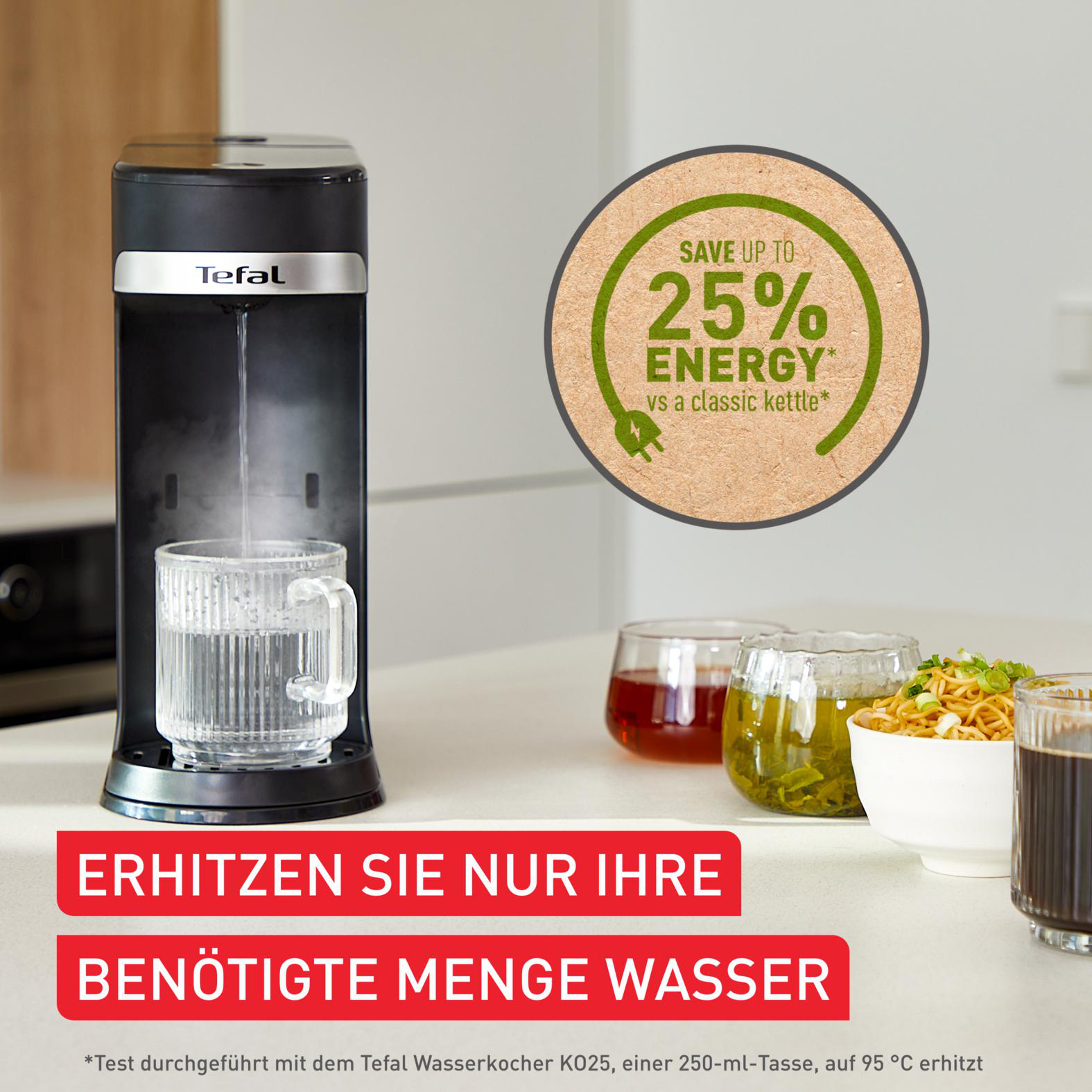 Schwarzer Tefal-Wasserkocher gießt Wasser in eine Glastasse. Andere Tassen und Nudeln stehen auf dem Tisch.