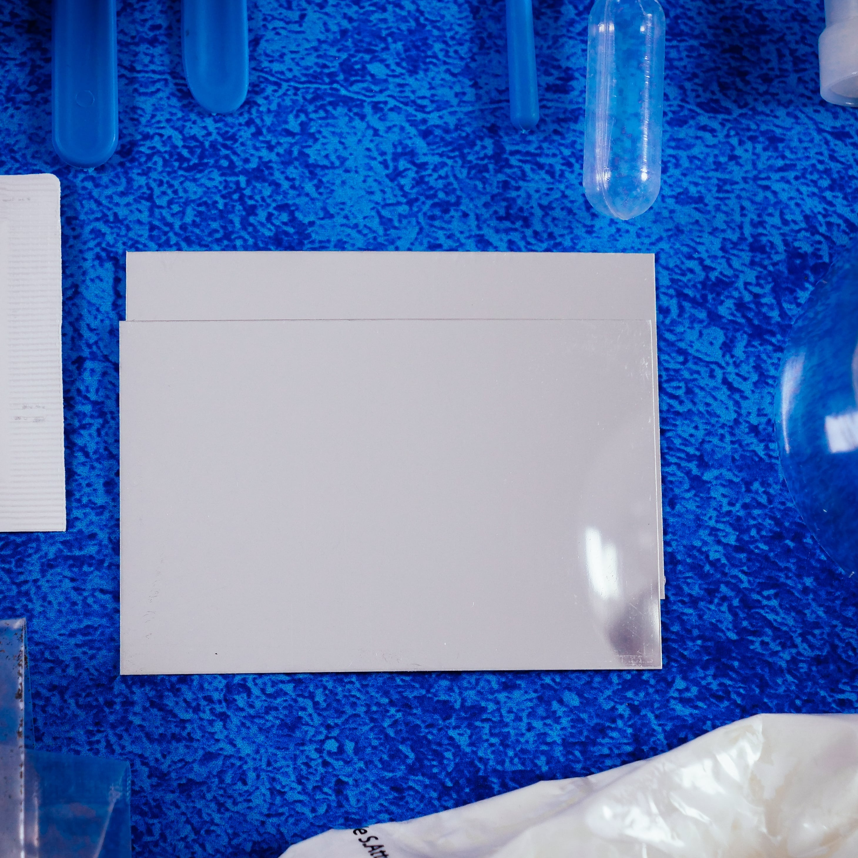 Obraz przedstawia sprzęt laboratoryjny, taki jak probówki i biała karta na niebieskim, teksturowanym tle.