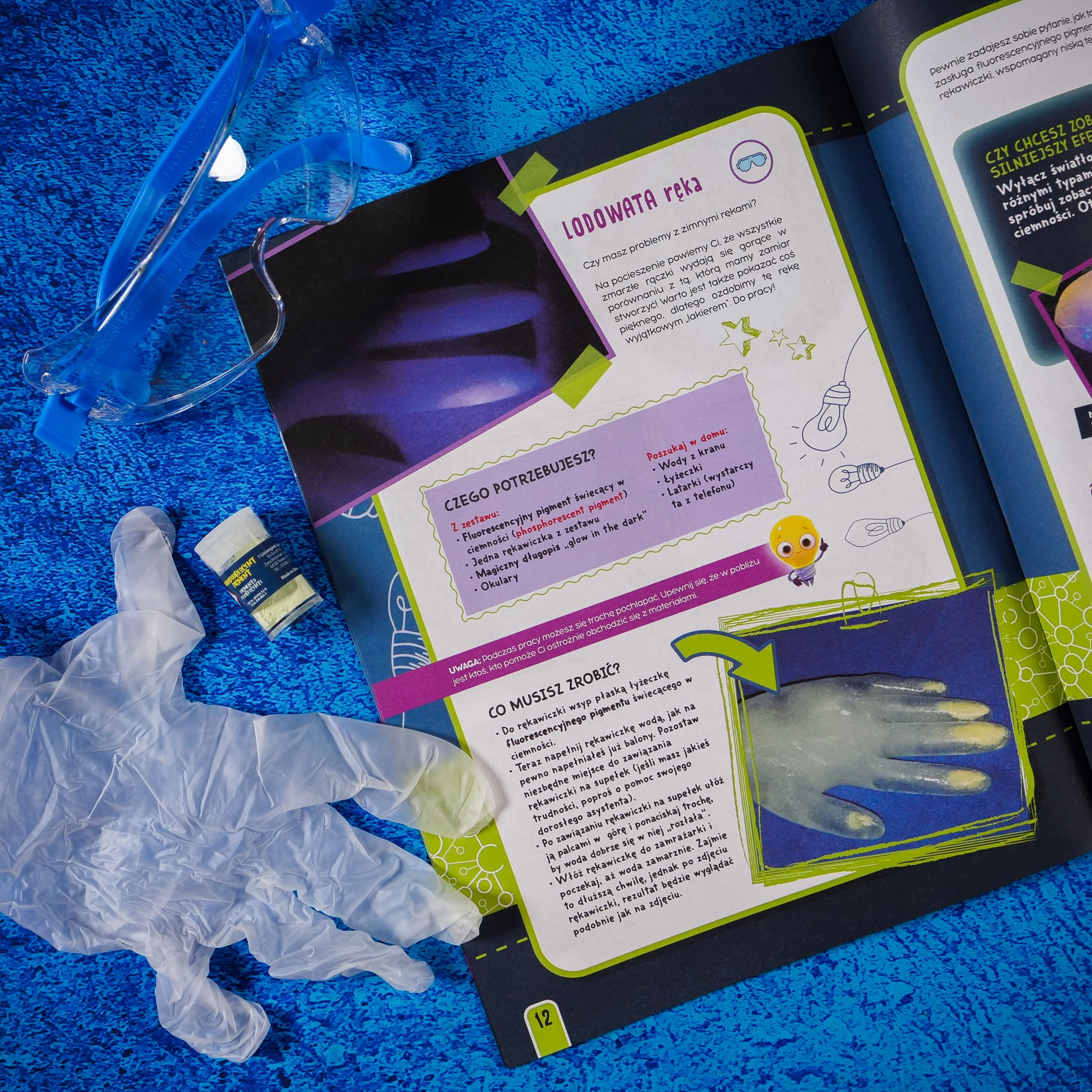 Niebieskie okulary ochronne, biała rękawica i żółty pojemnik z pigmentem na stronie książki.