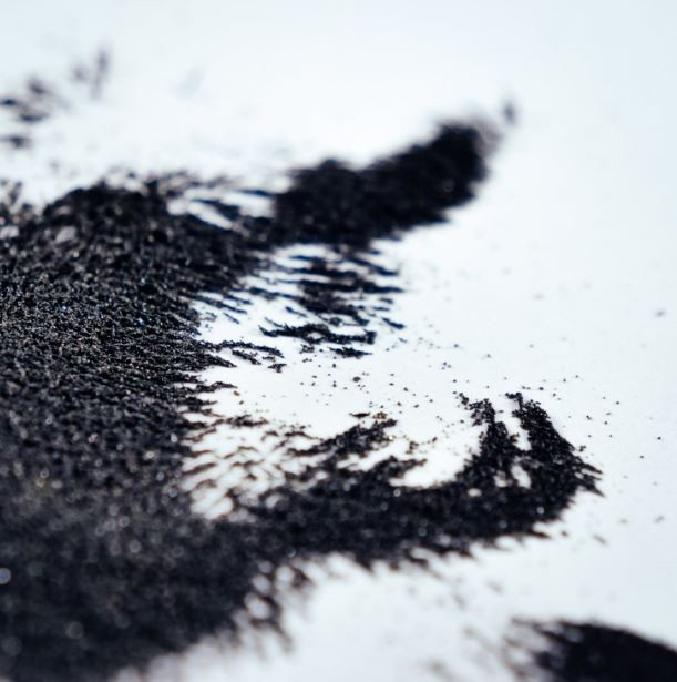 Zbliżenie czarnego proszku na białej powierzchni. Proszek tworzy nieregularny kształt z teksturowanymi detalami.