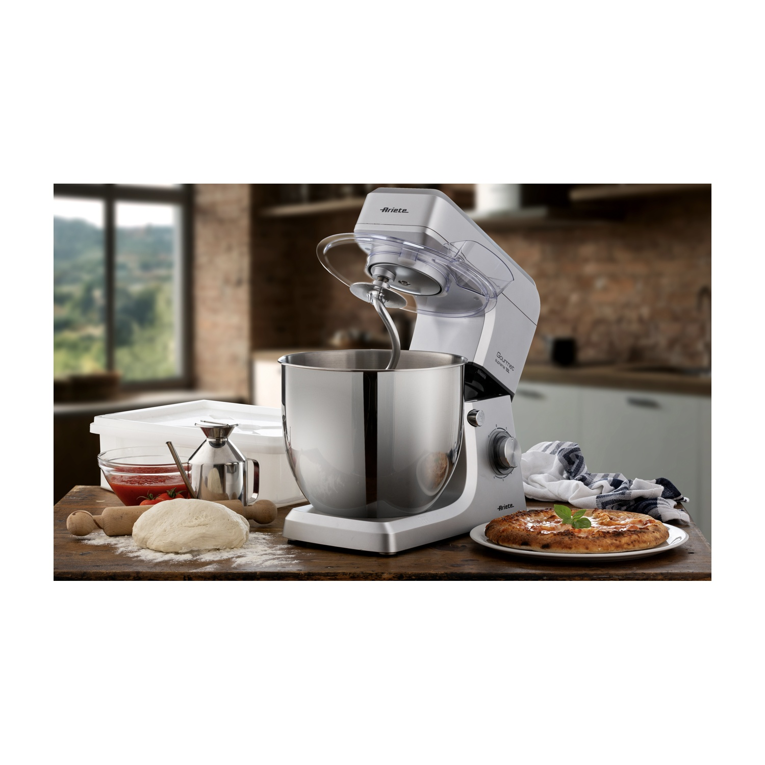 Scena di cucina con planetaria, impasto, pizza e ingredienti su un tavolo di legno. Sfondo: finestra e cucina.
