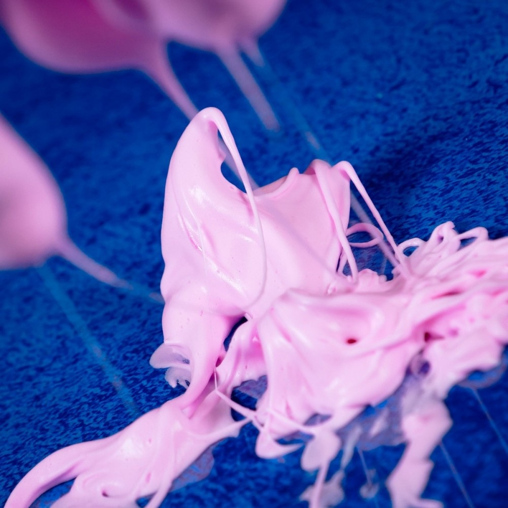 Różowa, wirująca substancja na niebieskiej powierzchni. Róż wygląda na gęsty, prawdopodobnie ubity topping. Niebieskie tło jest teksturowane.