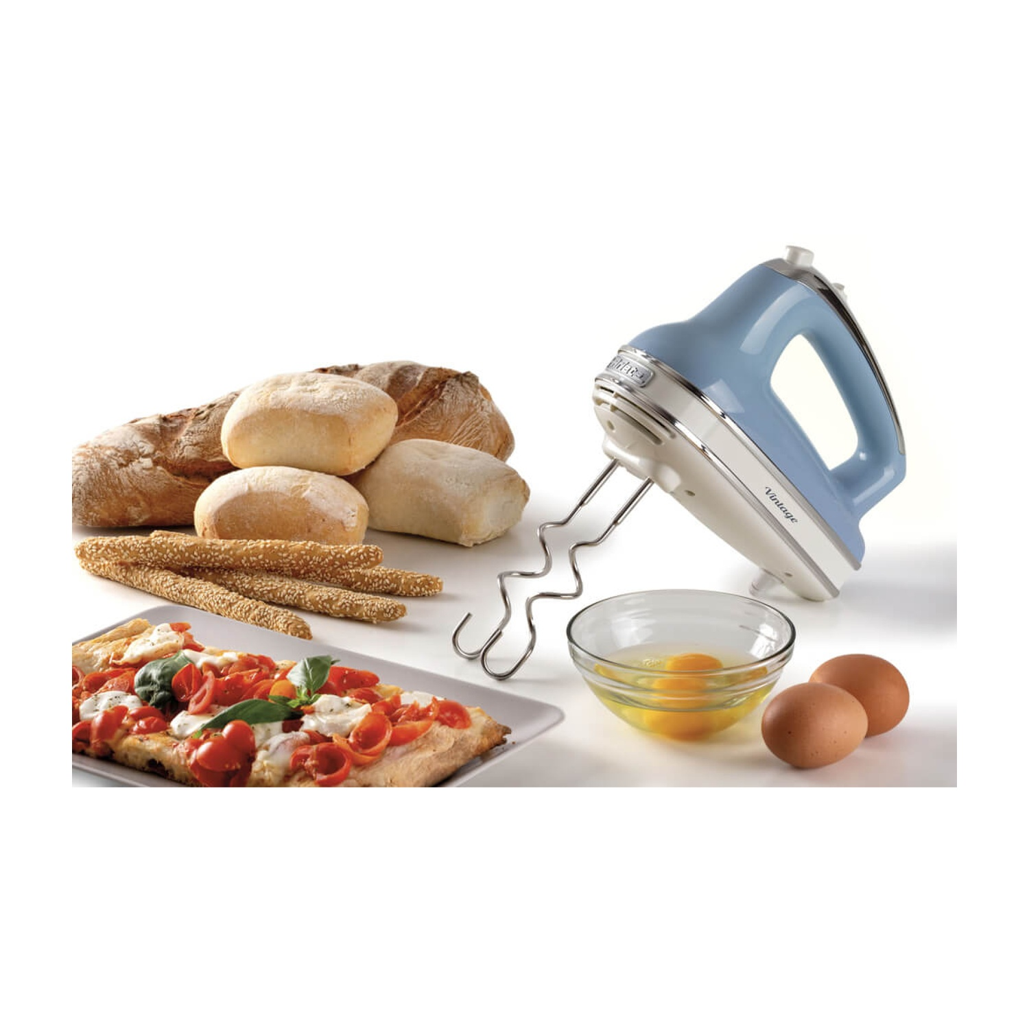 Un mixer azzurro chiaro con pane, pizza, uova e grissini su una superficie bianca. La scena è ben illuminata e appetitosa.